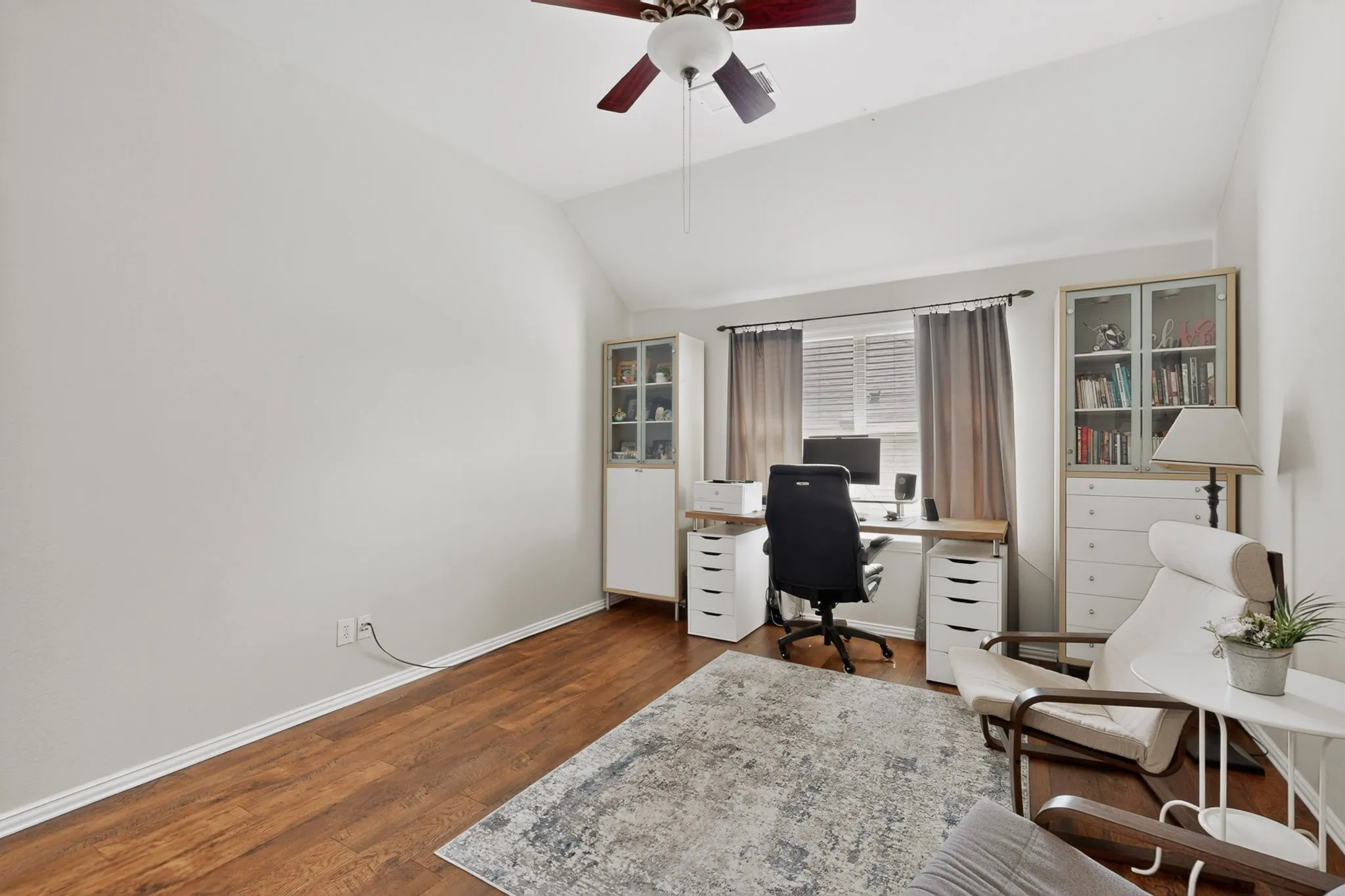 Spacious room featuring wood-finish flooring, a vaulted ceiling, and a ceiling fan