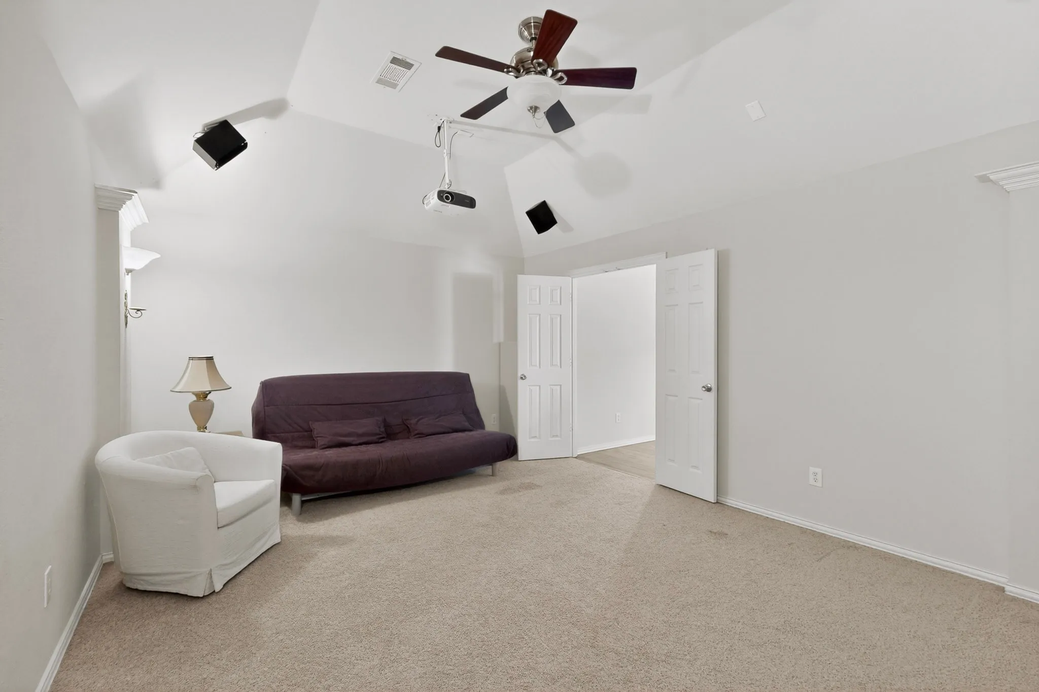 Carpeted room featuring a vaulted ceiling with a ceiling fan, built-in recessed speakers, and a mounted projector