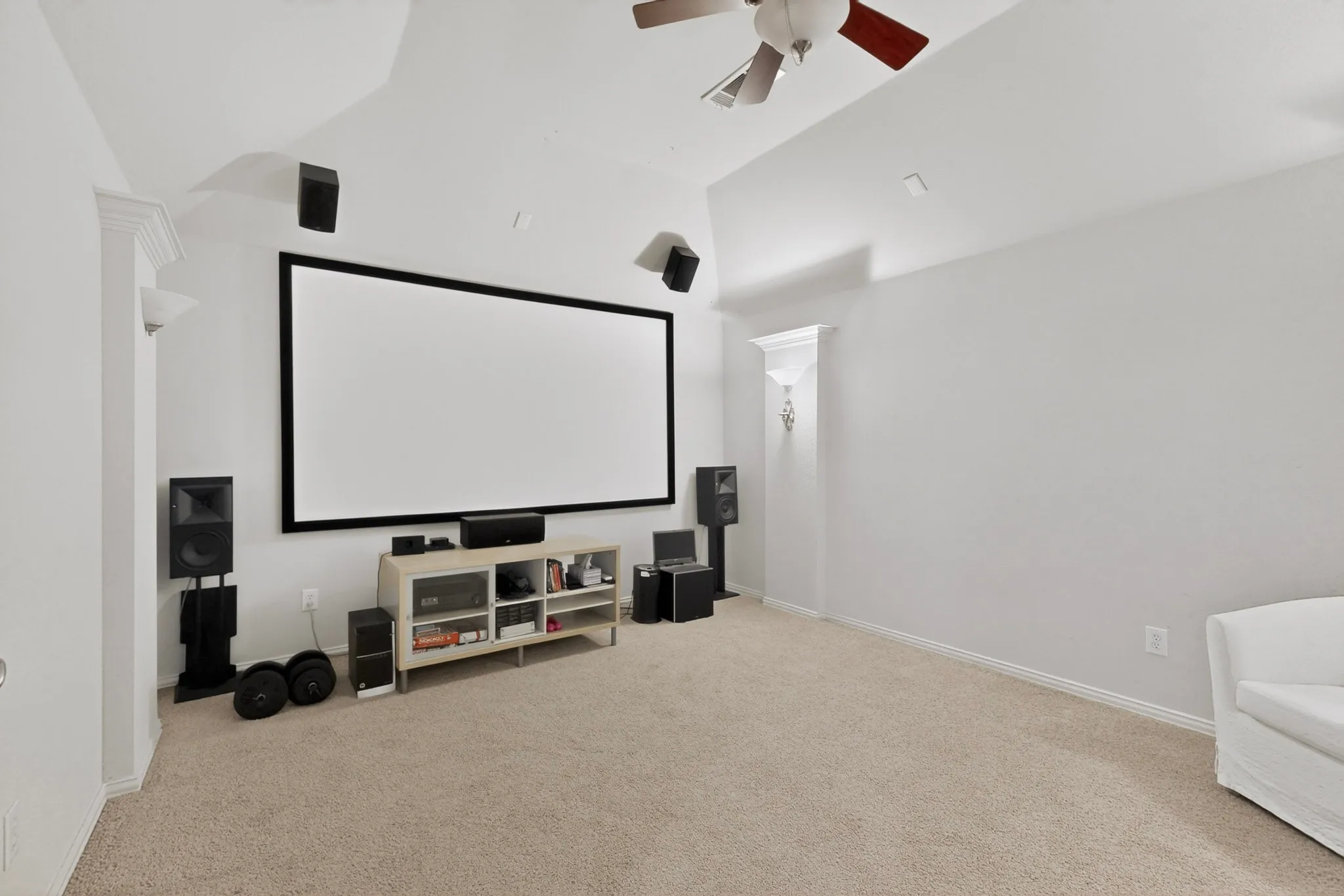 Dedicated media room featuring a large projection screen, high vaulted ceiling, and neutral-tone carpeting