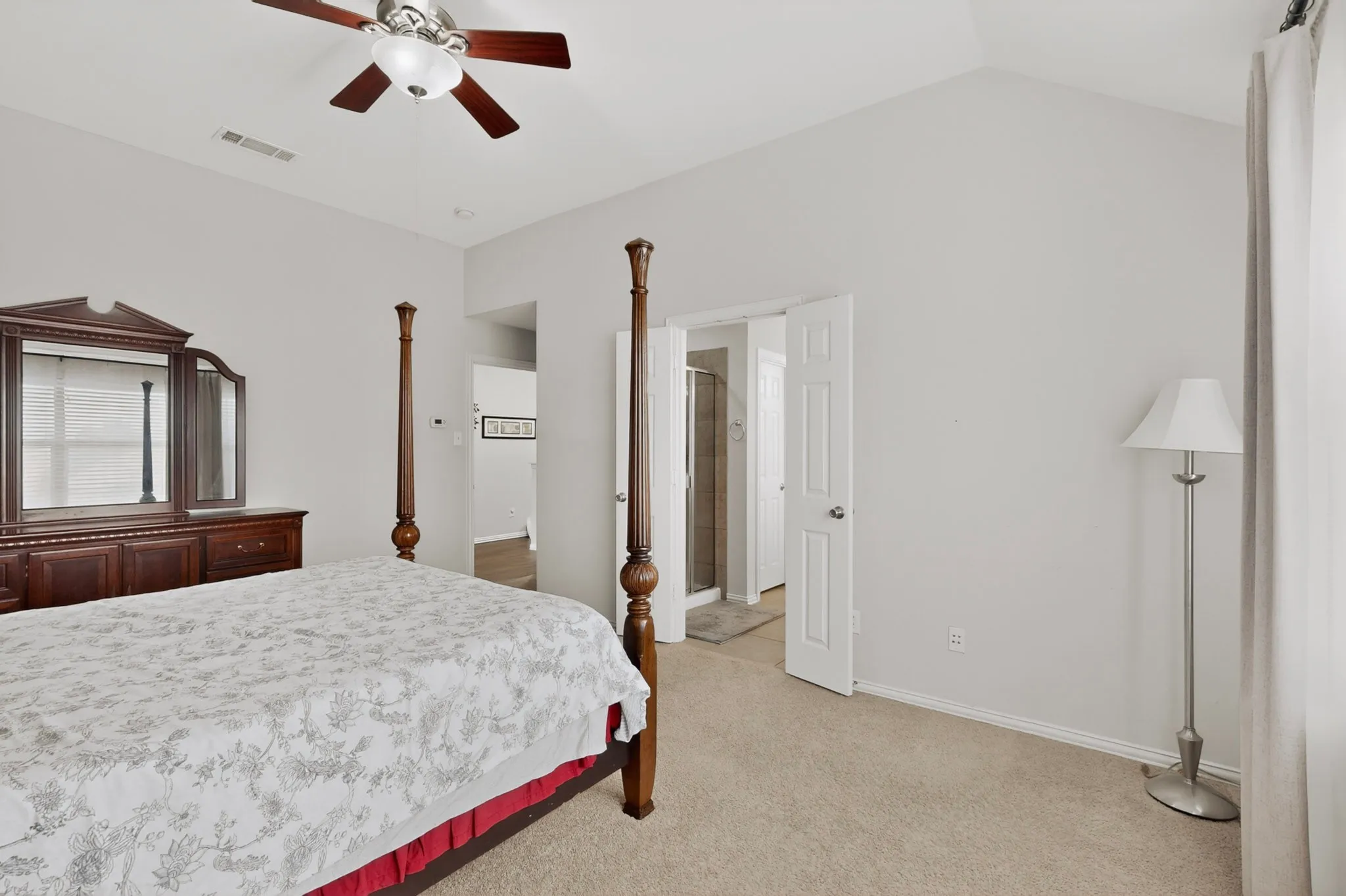Vaulted ceiling bedroom with a ceiling fan, carpet flooring, and a doorway opening to an additional space