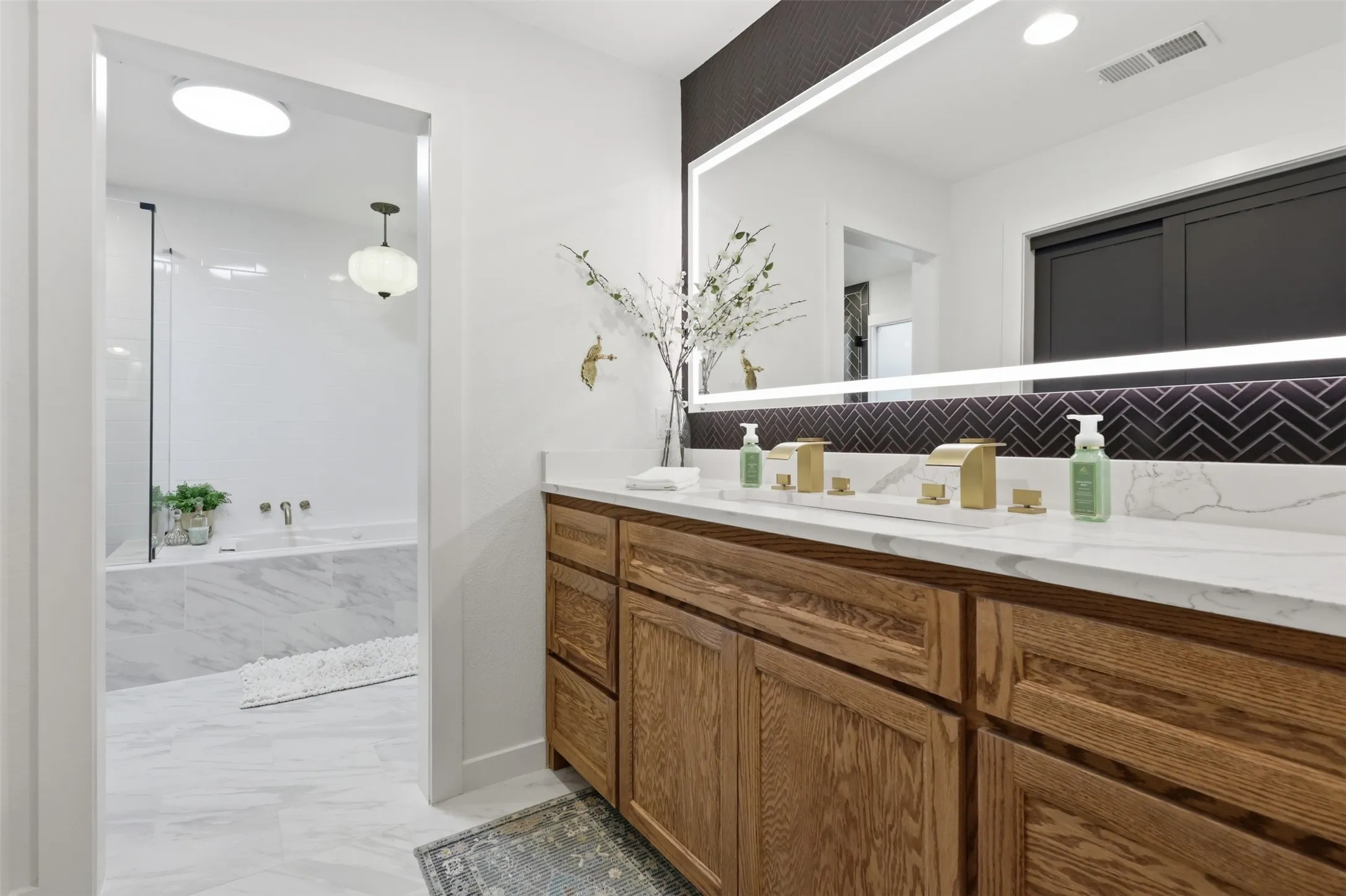 Completely renovated primary bathroom with custom built-in cabinets, quartz countertop and dual faucets.  Black tile with lighted mirror make the space feel like a high end hotel.
