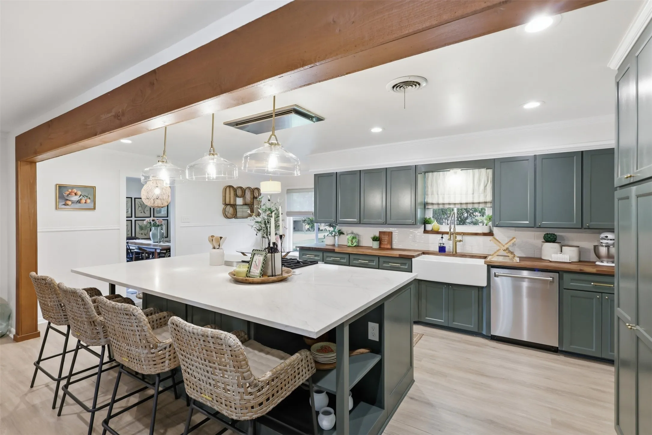 Kitchen features oversized island with cutouts for displaying dishes, quartz countertop, recessed lighting, farmhouse sink surrounded by butcher block countertops and painted cabinets with new shaker style faces and decorative hardware.