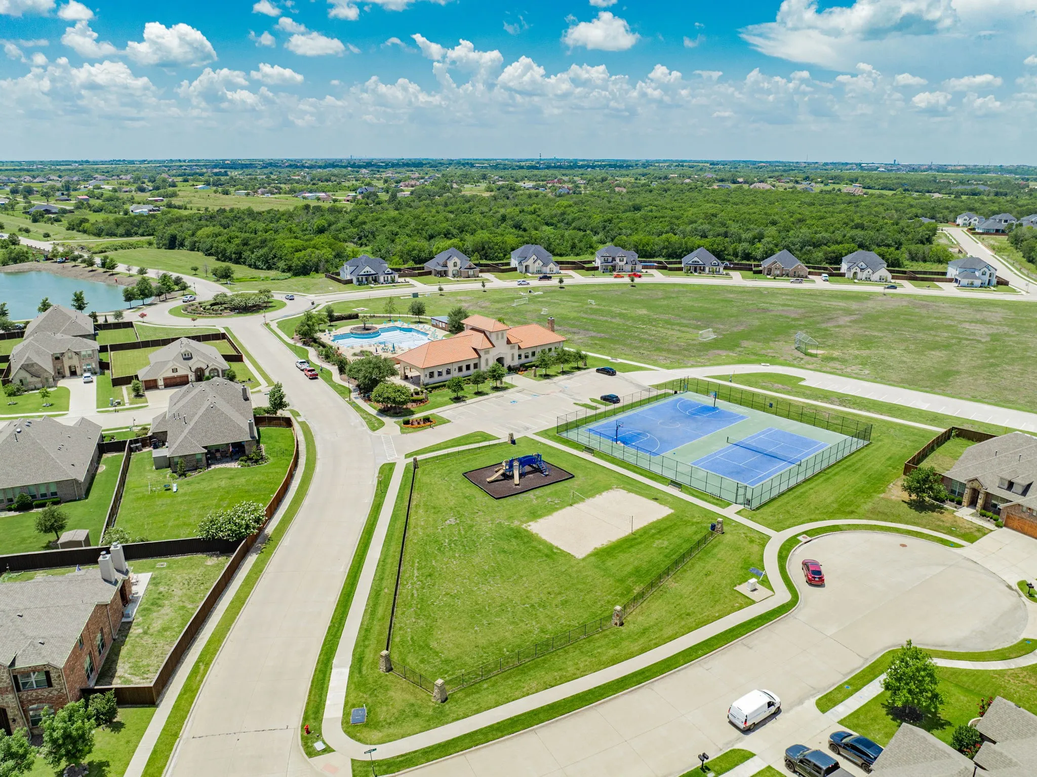 Aerial perspective showcasing a residential community with a central clubhouse, swimming pool, tennis courts, and playground