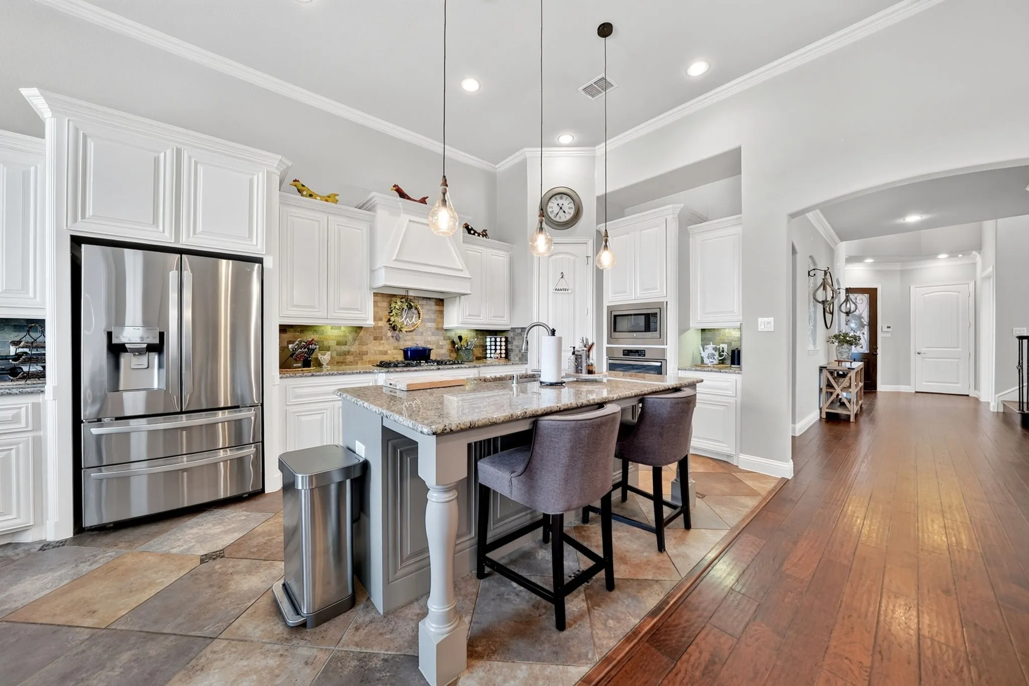 Kitchen featuring a central island with countertop seating, granite countertops, white cabinetry, stainless steel appliances, and a tile backsplash