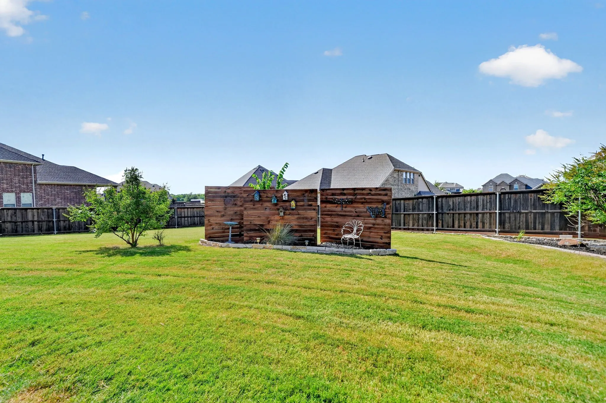 Expansive fenced backyard featuring a wood privacy screen, a small tree, and a lush green lawn