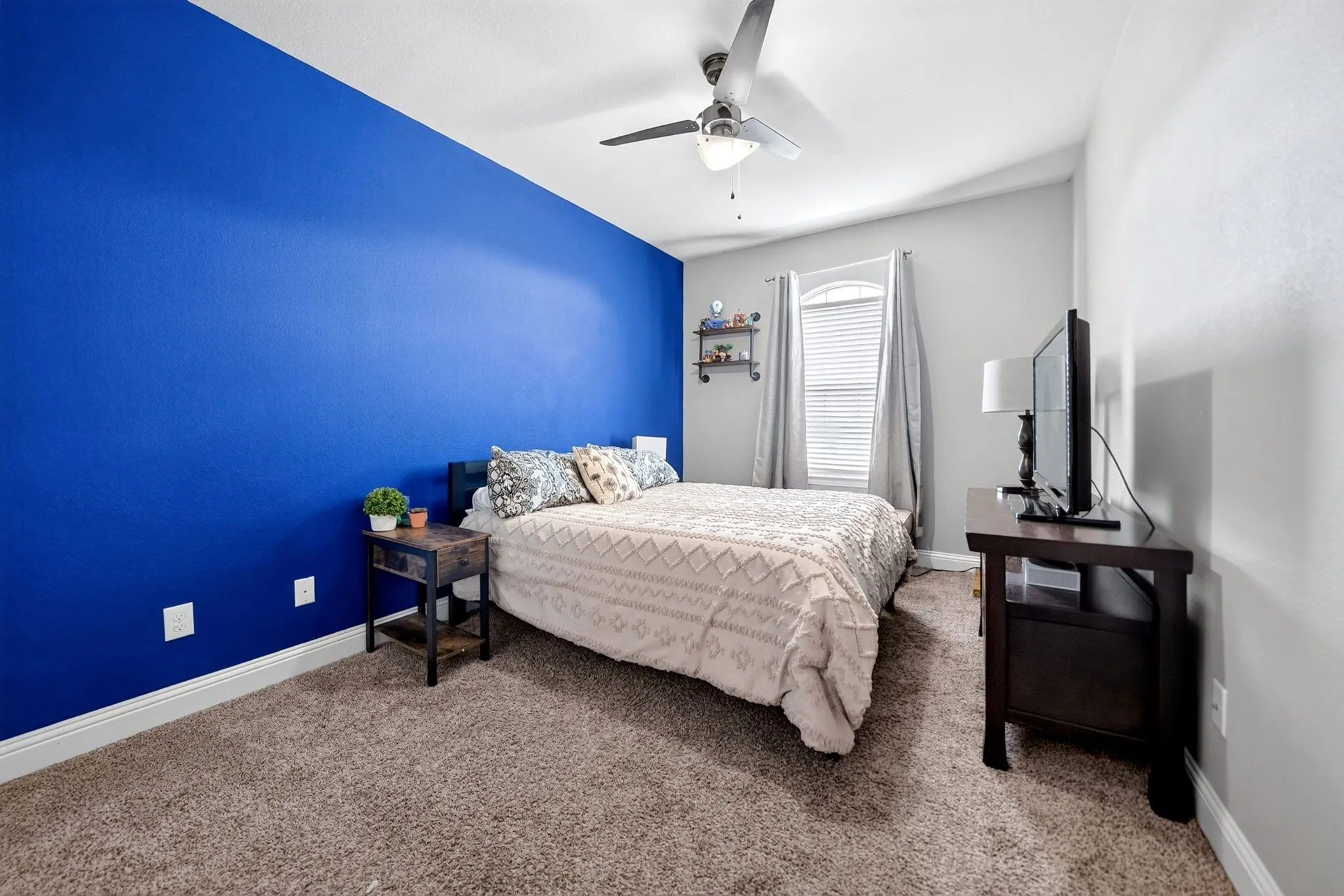 Carpeted room featuring a ceiling fan with integrated lighting, a window with blinds and drapes, and a accent wall