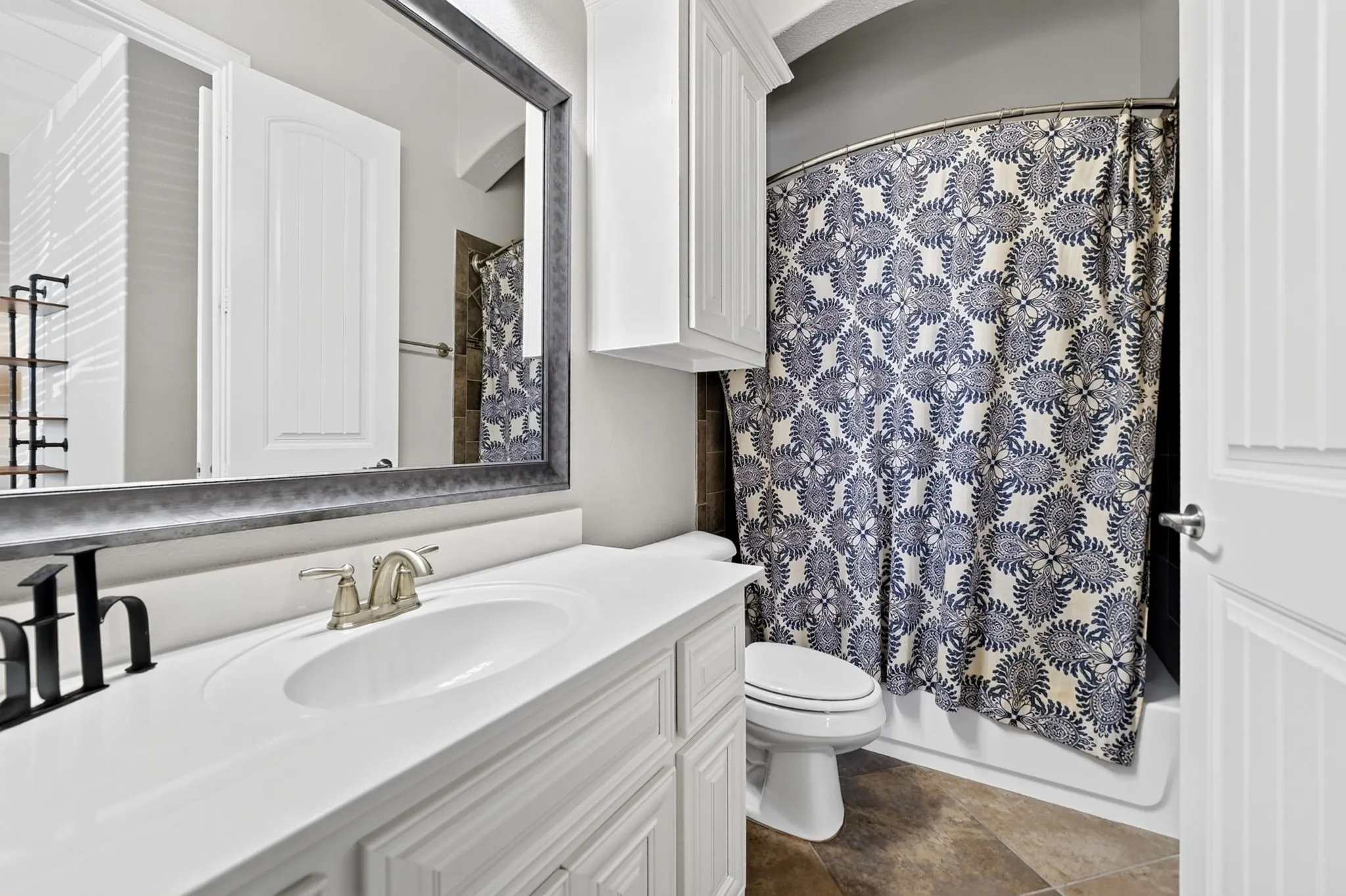 Bathroom featuring a single vanity with a white countertop and undermount sink, brushed nickel faucet, framed mirror, white cabinetry, and a tub-shower combination