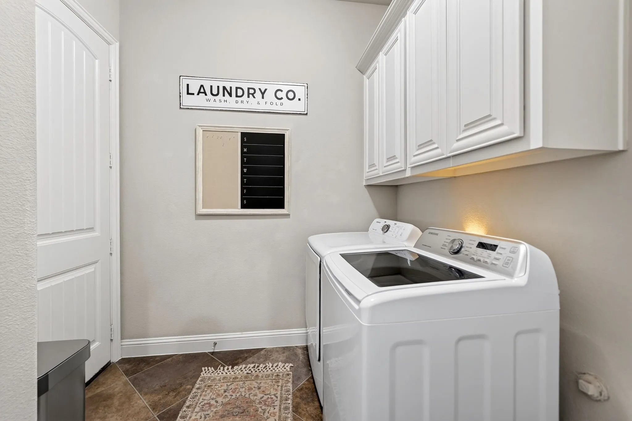 Utility space featuring upper cabinetry with crown molding, a paneled door, and large format floor tiling
