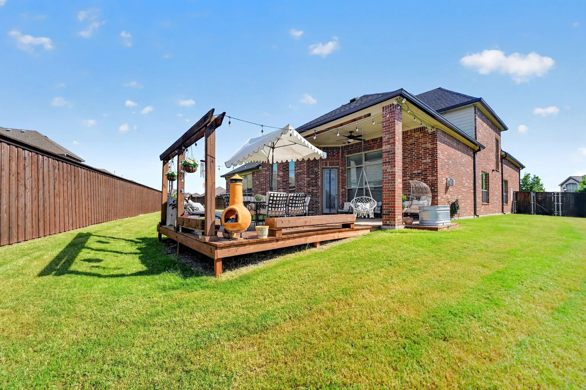 Spacious backyard with a multi-level wooden deck featuring a pergola, string lighting, and direct access to the interior