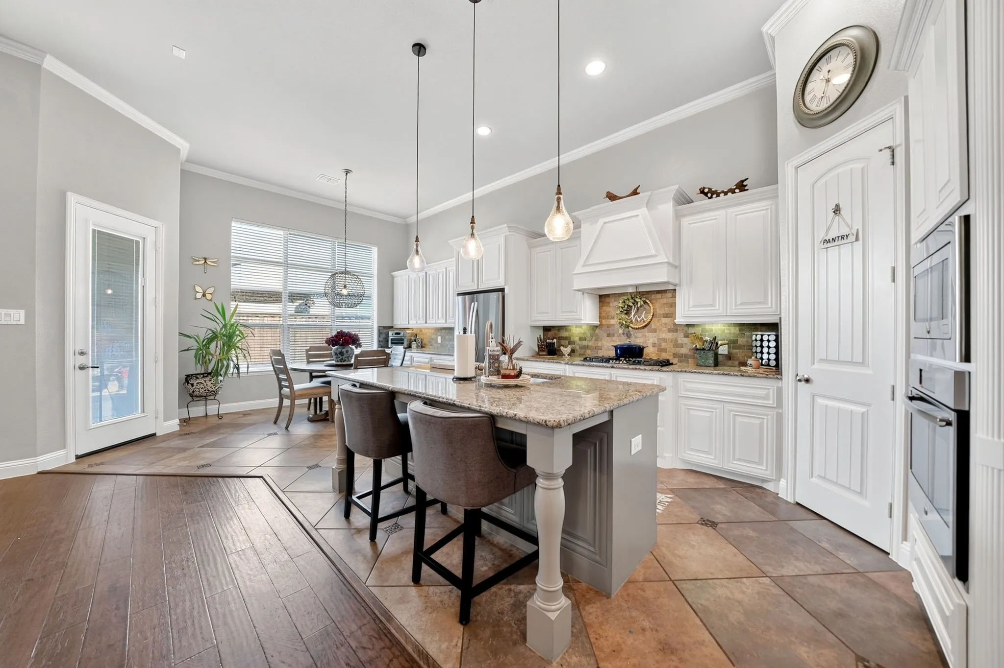 Spacious kitchen featuring an expansive center island with granite countertop, white cabinetry with crown molding, stainless steel built-in appliances, and a tiled backsplash