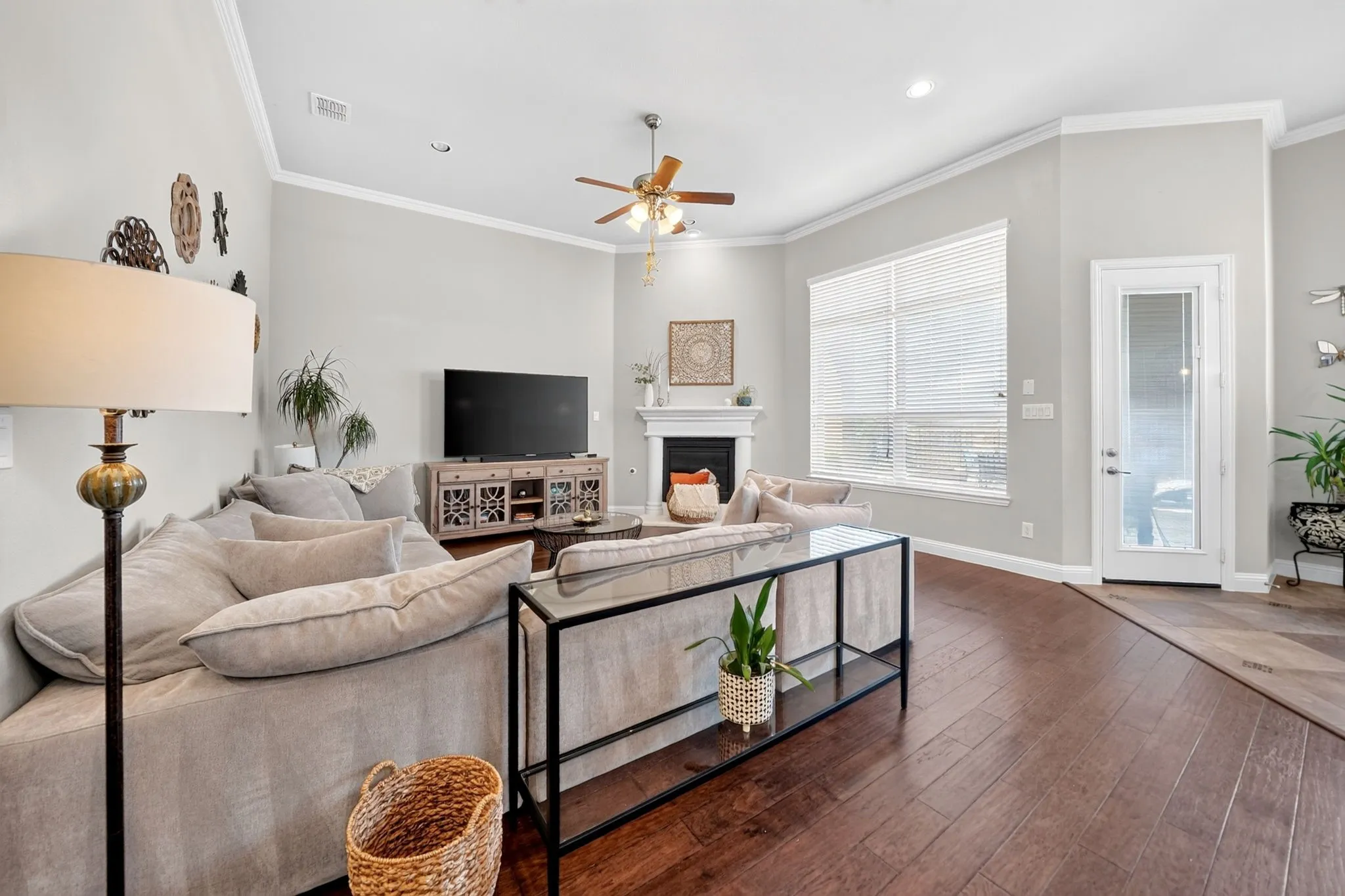 Spacious living area featuring rich wood-finish flooring, a white mantel fireplace, extensive crown molding, and a ceiling fan