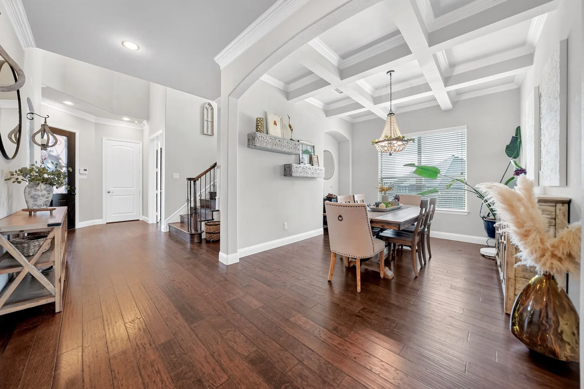 Hardwood flooring extends throughout this open-concept space, featuring a dining area with a coffered ceiling and a chandelier