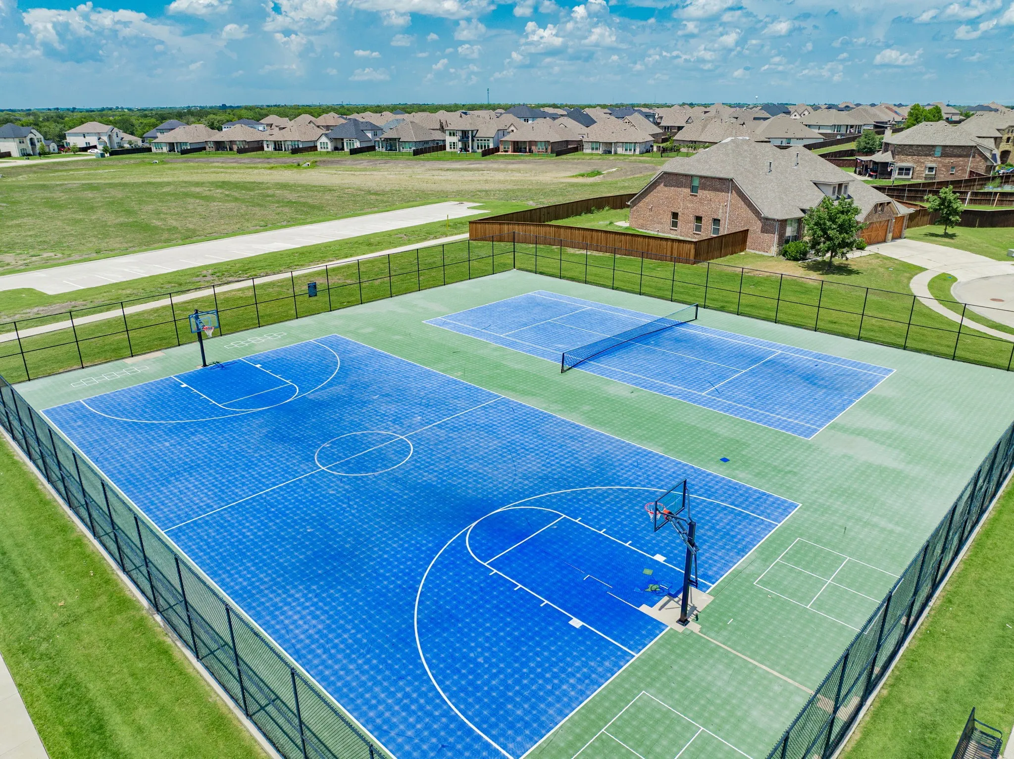 Multi-sport court featuring a full basketball court and a tennis court, both enclosed by a black metal fence