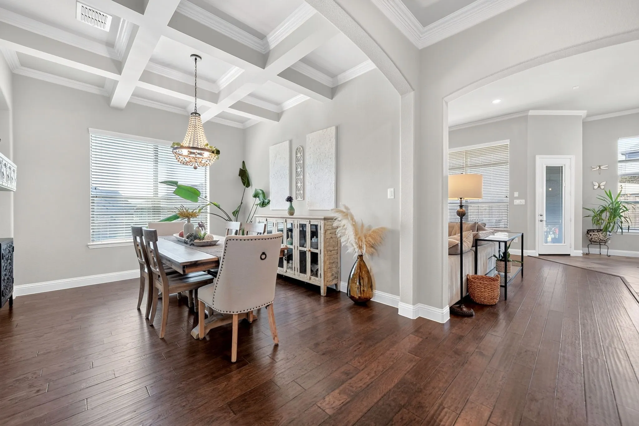 Coffered ceiling dining area featuring wood-finish flooring, a crystal chandelier, and a large window with​​‌​​​​‌​​‌‌​‌‌​​​‌‌​‌​‌​‌​​​‌​​ blinds