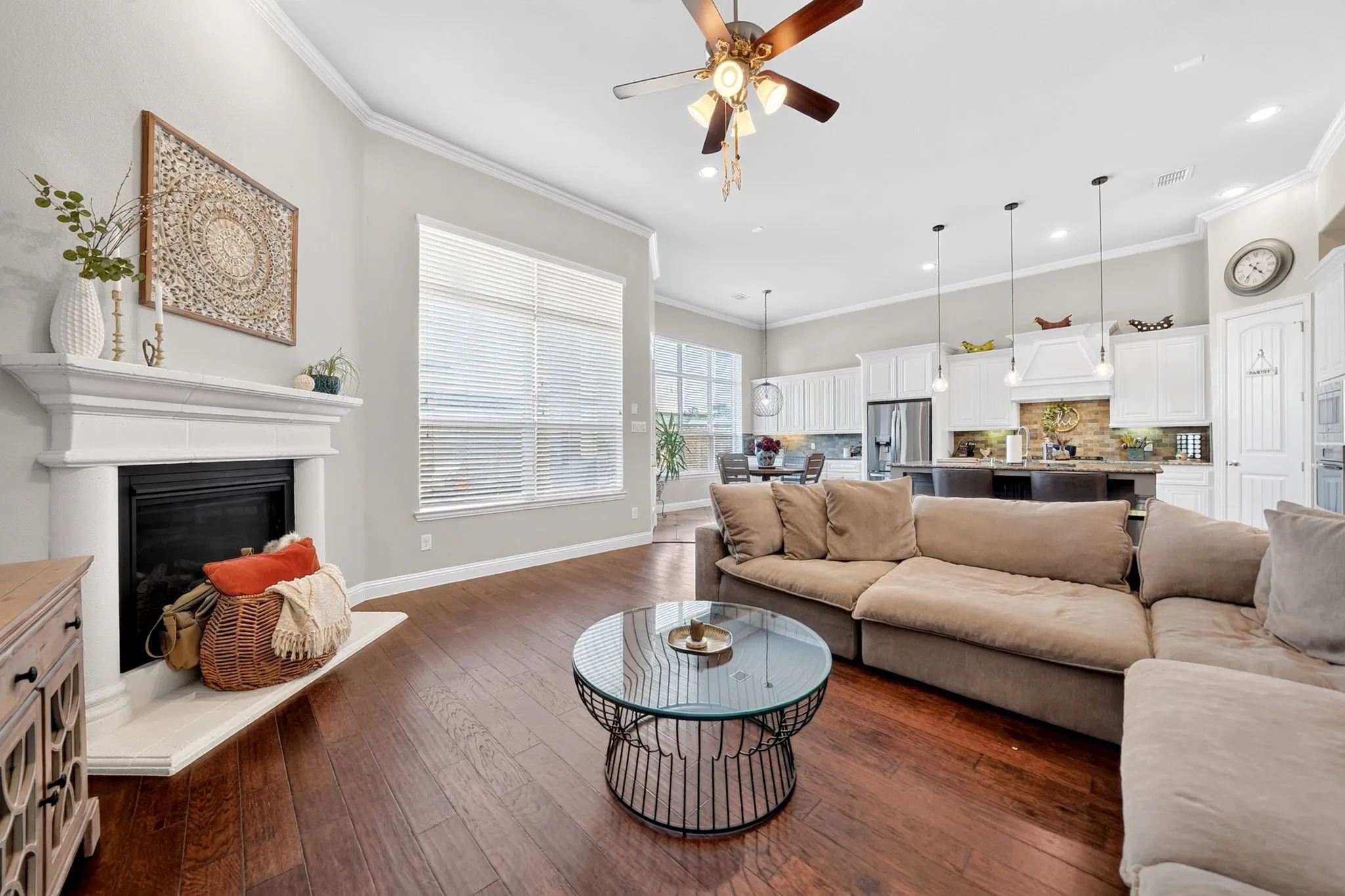Open-concept living space featuring wood-finish flooring, a white mantel fireplace, and a large window with blinds