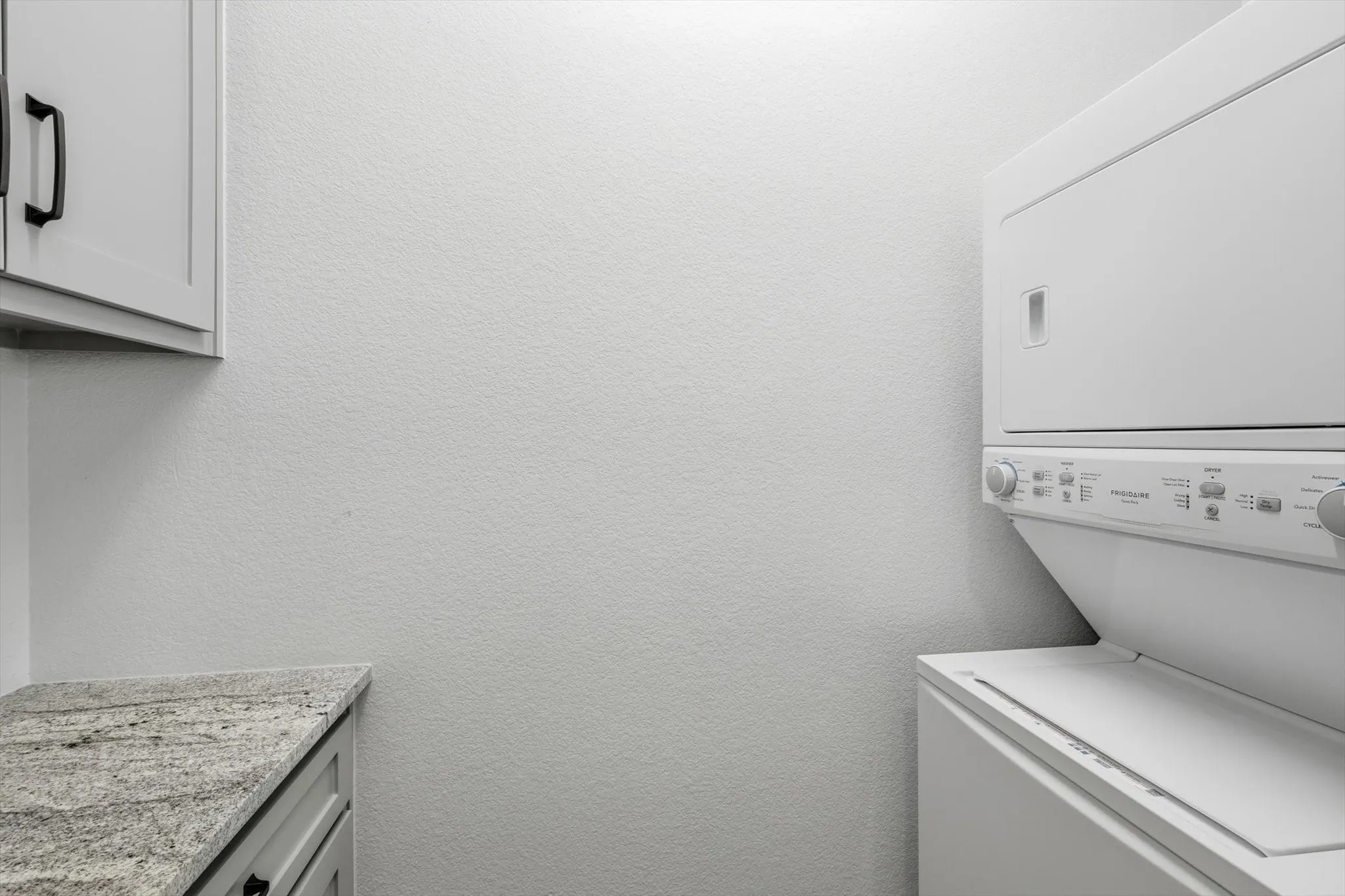 Guest Home - Laundry area featuring a stacked washer and dryer, light gray cabinetry with black hardware, and a stone-finish countertop