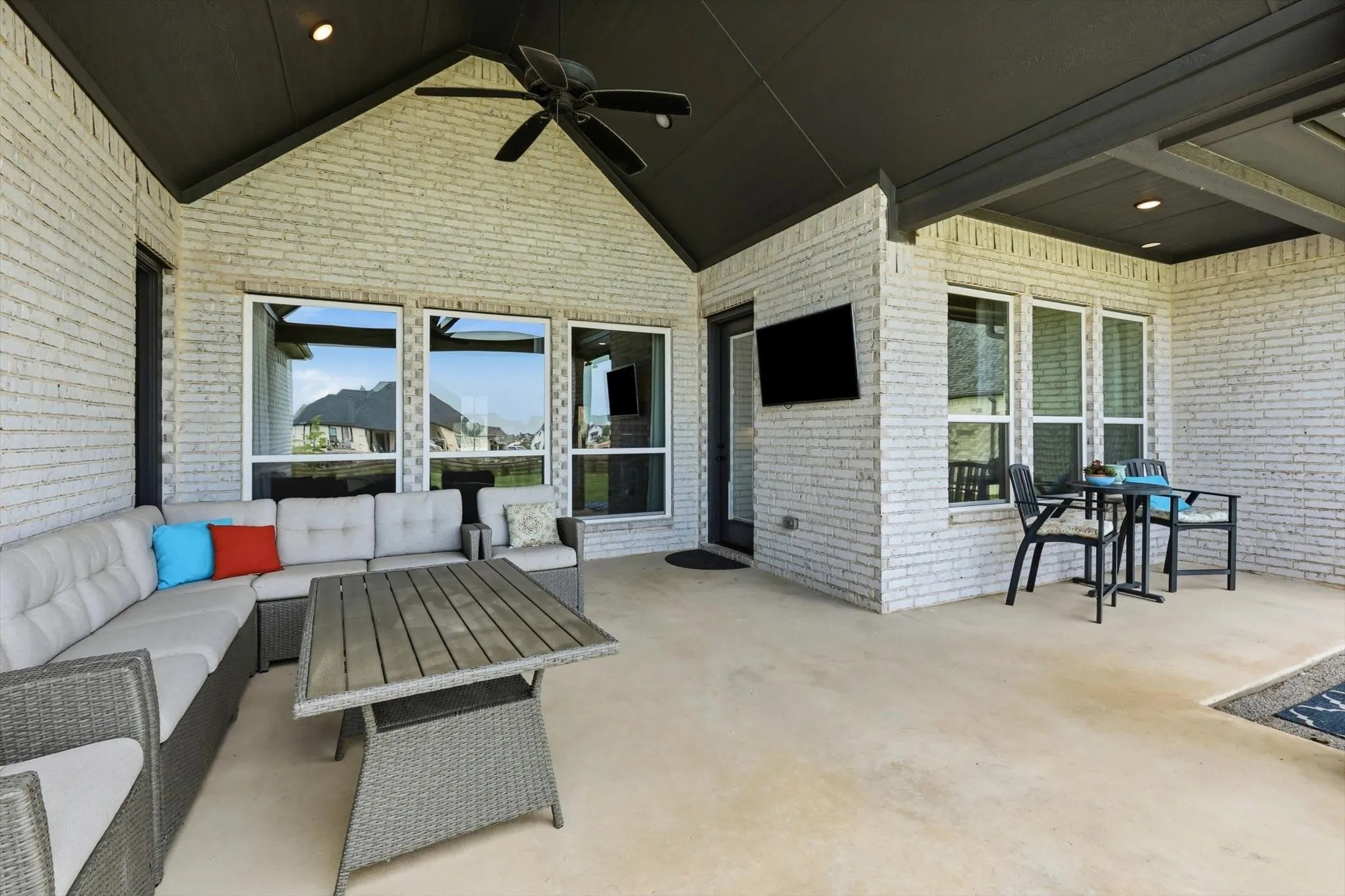 Covered patio featuring white brick exterior walls and a dark vaulted ceiling