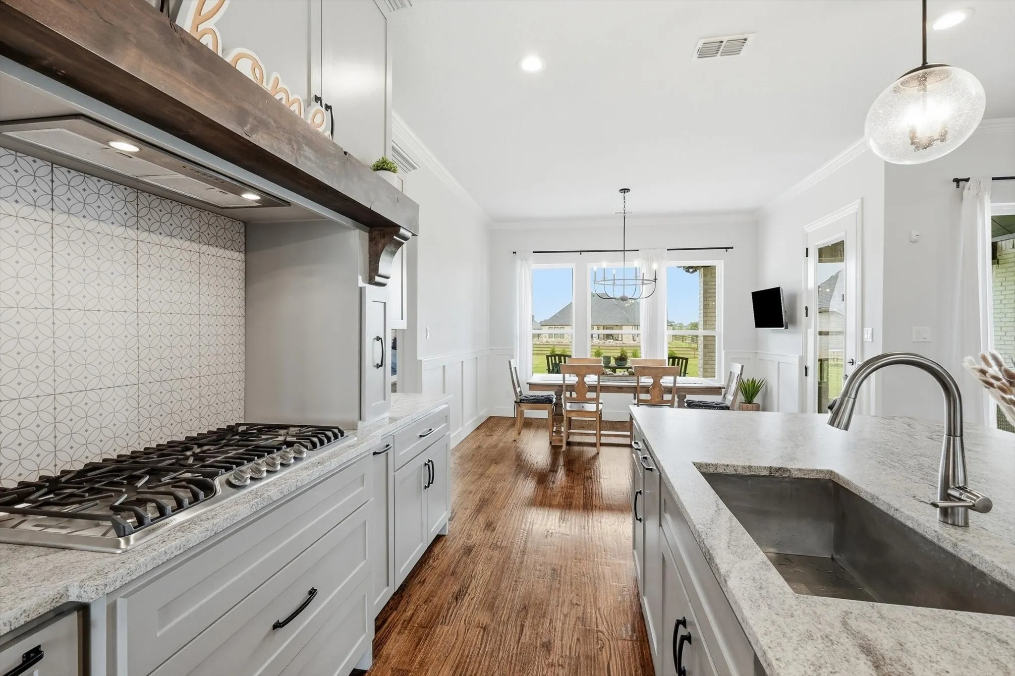 Gourmet kitchen featuring a built-in gas range with decorative hood, light gray cabinetry, and granite countertops