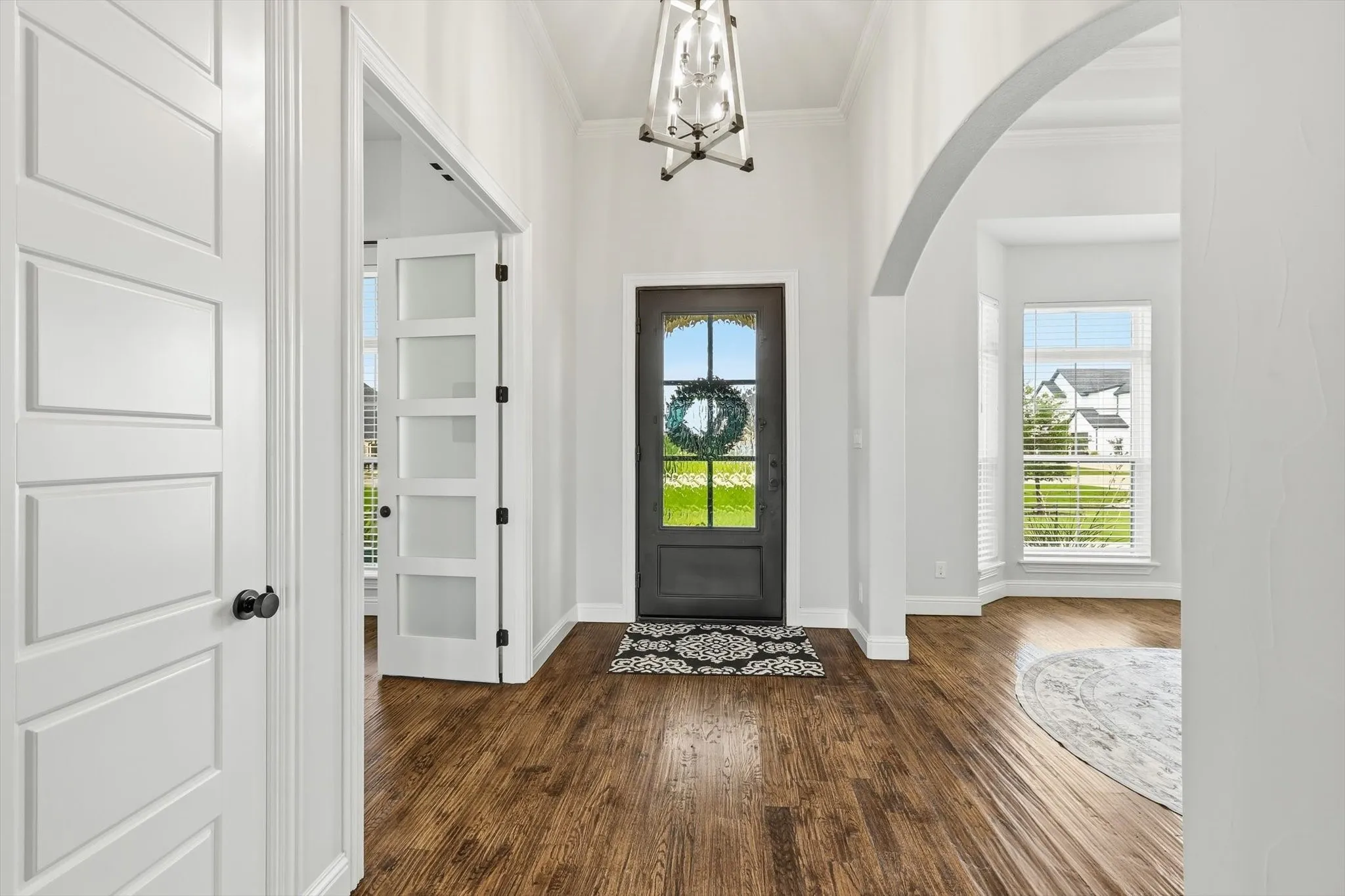 Entryway featuring wood-finish flooring, a contemporary overhead light fixture, and a dark-paneled front door with arched glass