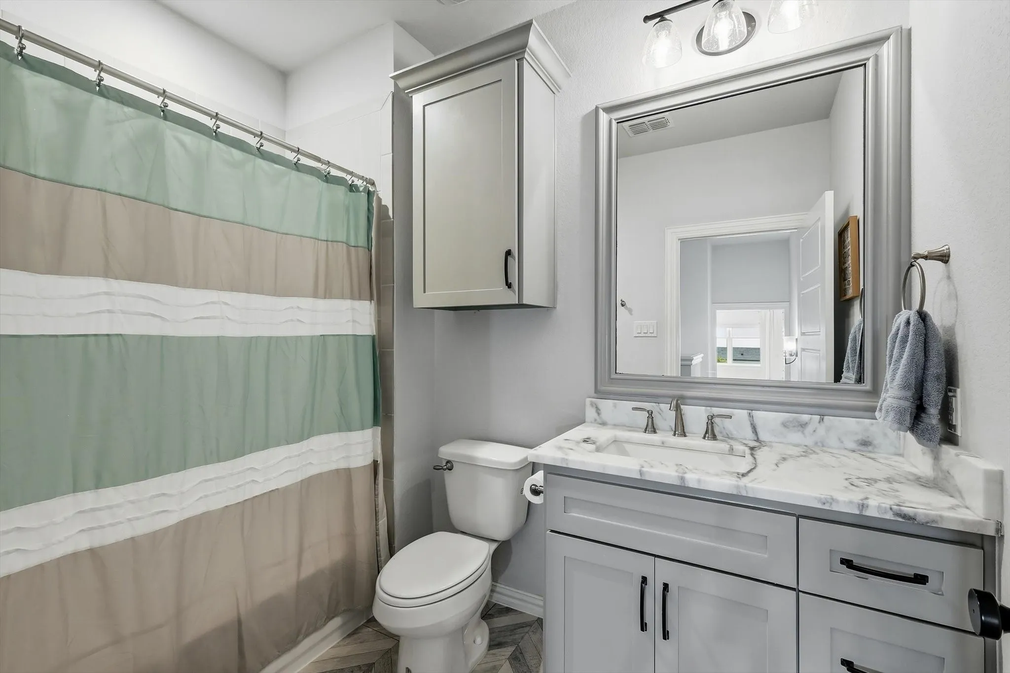 Upstairs bathroom featuring a single vanity with a patterned countertop, gray cabinetry with dark hardware, a framed mirror, and a wall-mounted light fixture