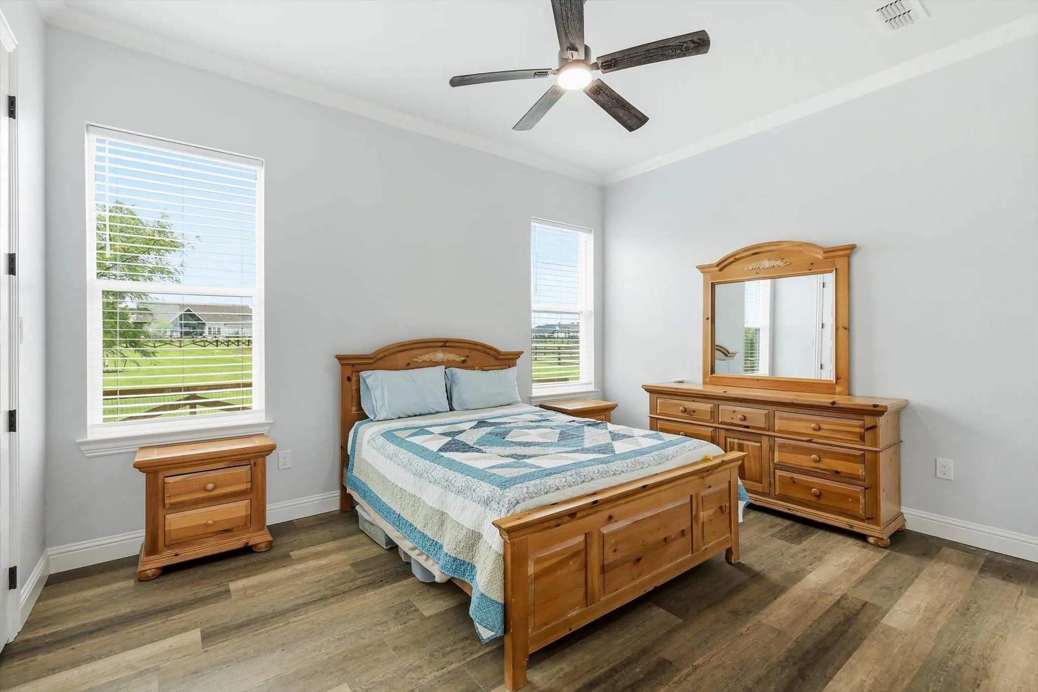 Guest Home - Spacious room featuring wood-finish flooring, two large windows with blinds, and a ceiling fan