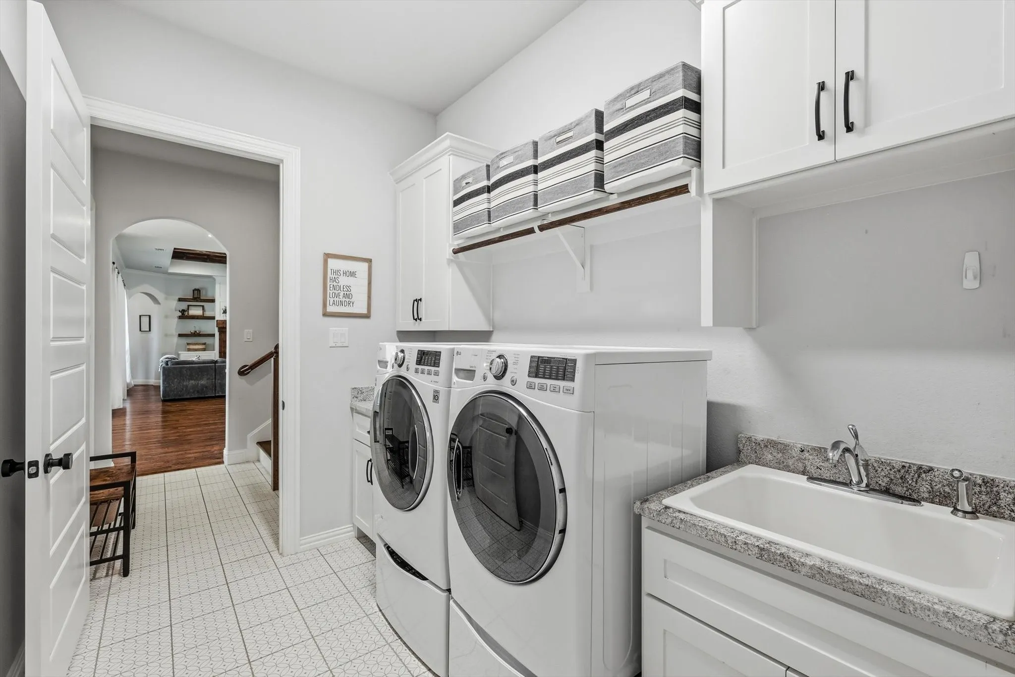 Dedicated laundry room with direct access to Primary bedroom featuring white shaker-style cabinetry, a utility sink with a stone-finish countertop, and white tile flooring