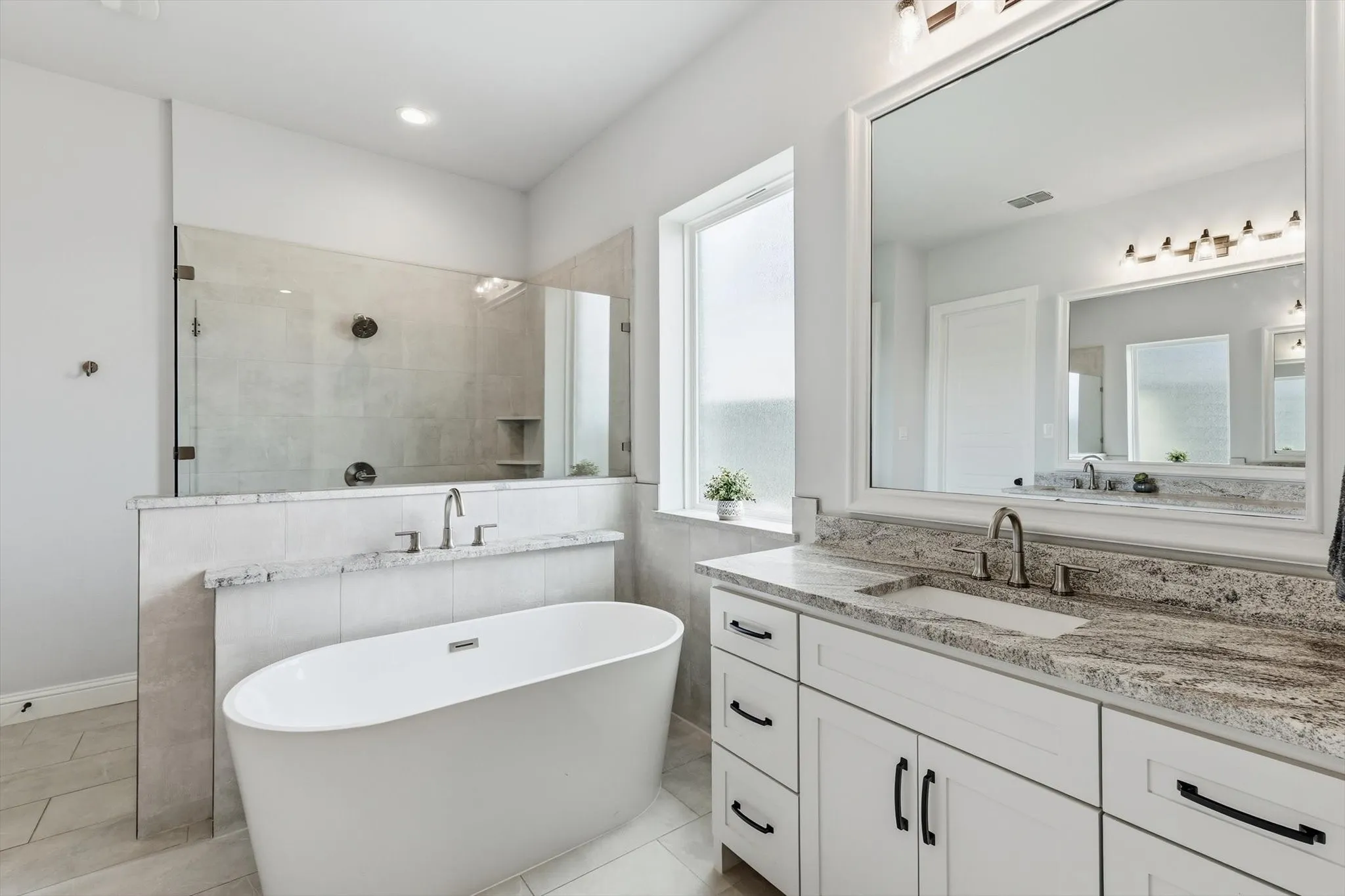 Contemporary bathroom featuring a freestanding soaking tub, a large walk-in shower with glass enclosure, a white double vanity with stone countertops, and a frosted window