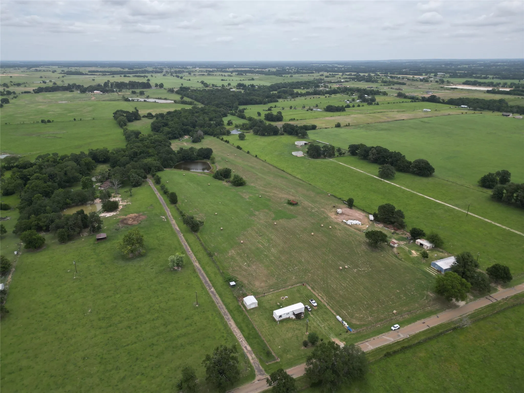 Expansive agricultural property featuring multiple structures, verdant fields, and two distinct ponds