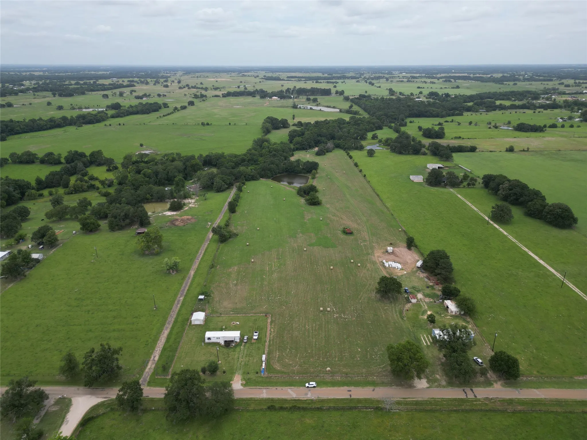 Expansive rural landscape featuring extensive green pastures, scattered mature trees, and a visible pond