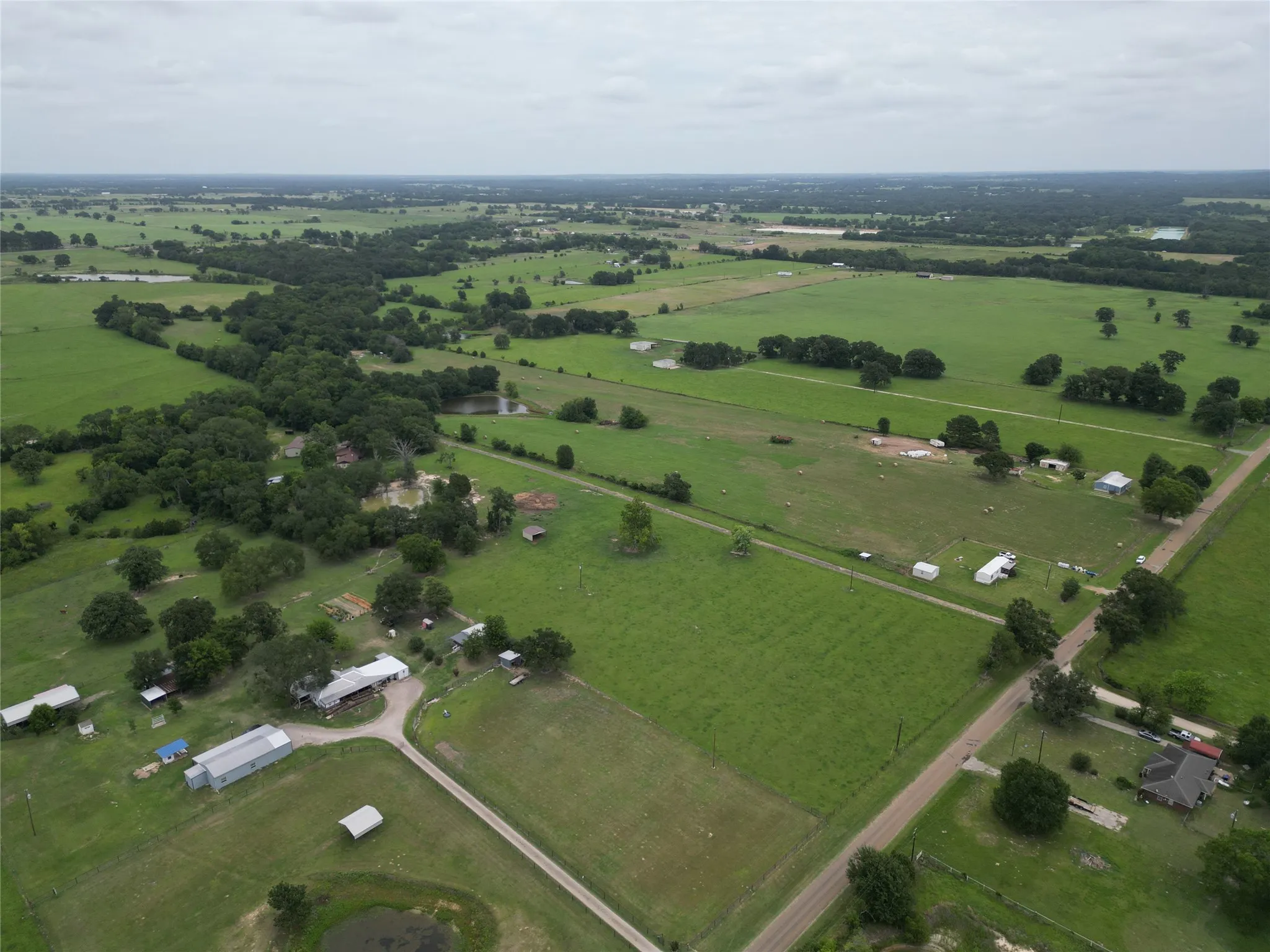 Expansive rural landscape featuring extensive green pastures, mature trees, and multiple outbuildings