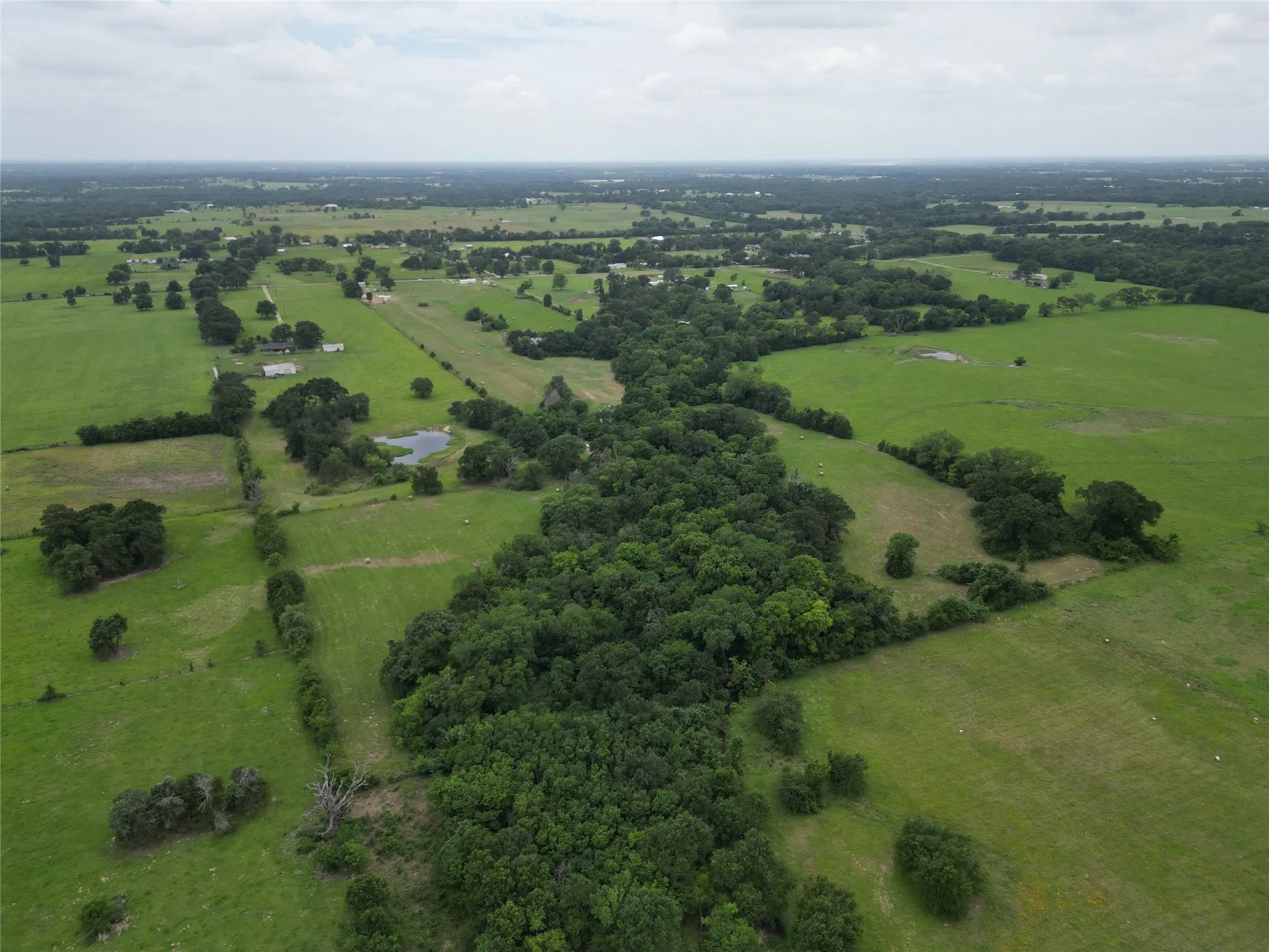 Expansive rural landscape featuring a mix of open fields, wooded areas, and a visible pond