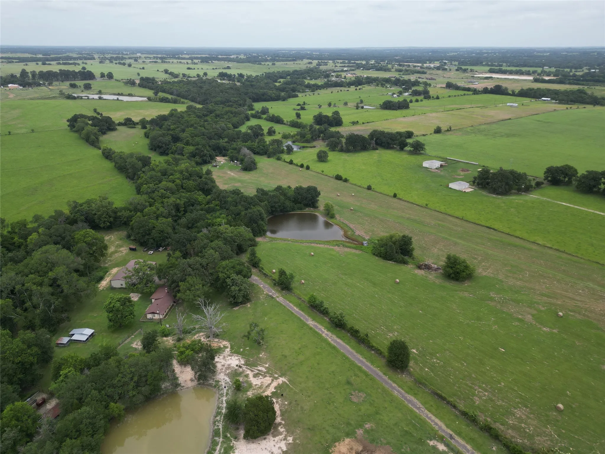 Expansive rural landscape featuring multiple ponds, abundant mature trees, open fields, and distant structures