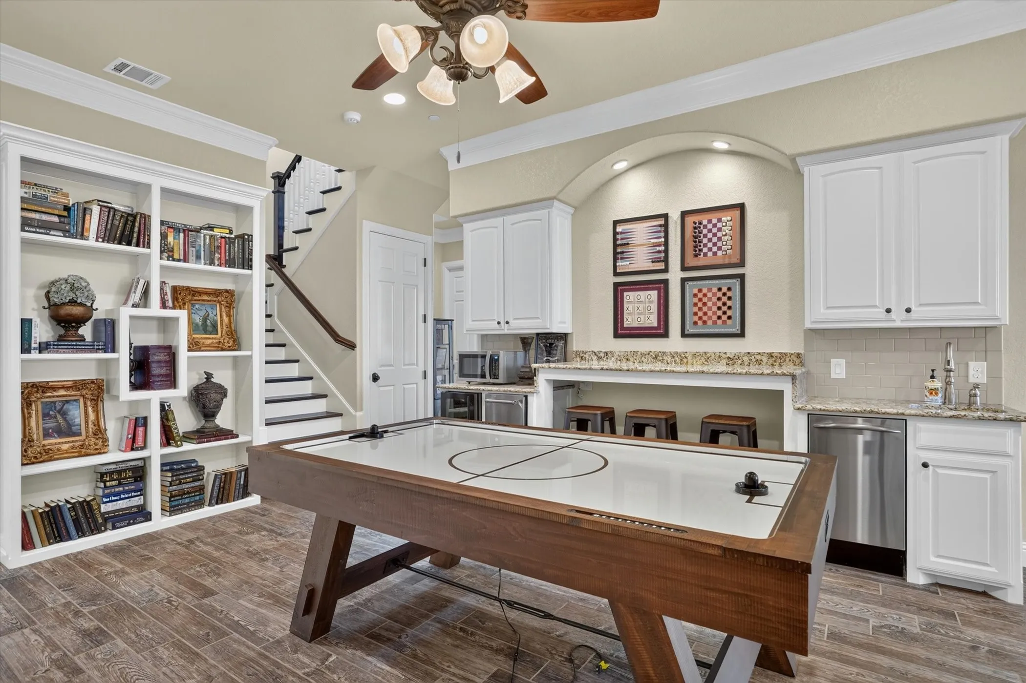 Entertainment area featuring wood-finish flooring, built-in shelving, a wet bar with granite-style countertops, and white cabinetry