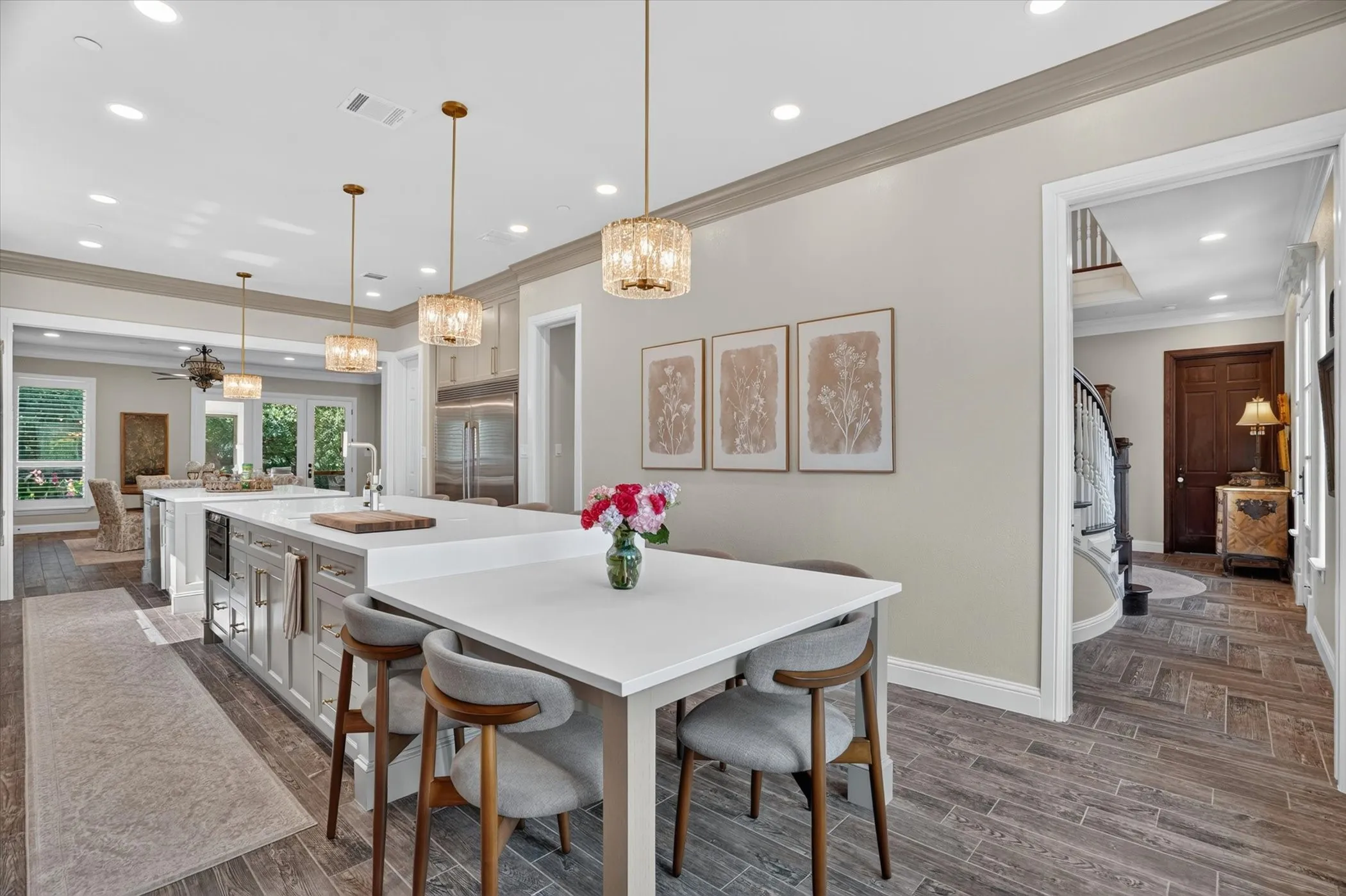 Spacious kitchen featuring an expansive central island with integrated seating, white countertops, and wood-finish flooring laid in a herringbone pattern