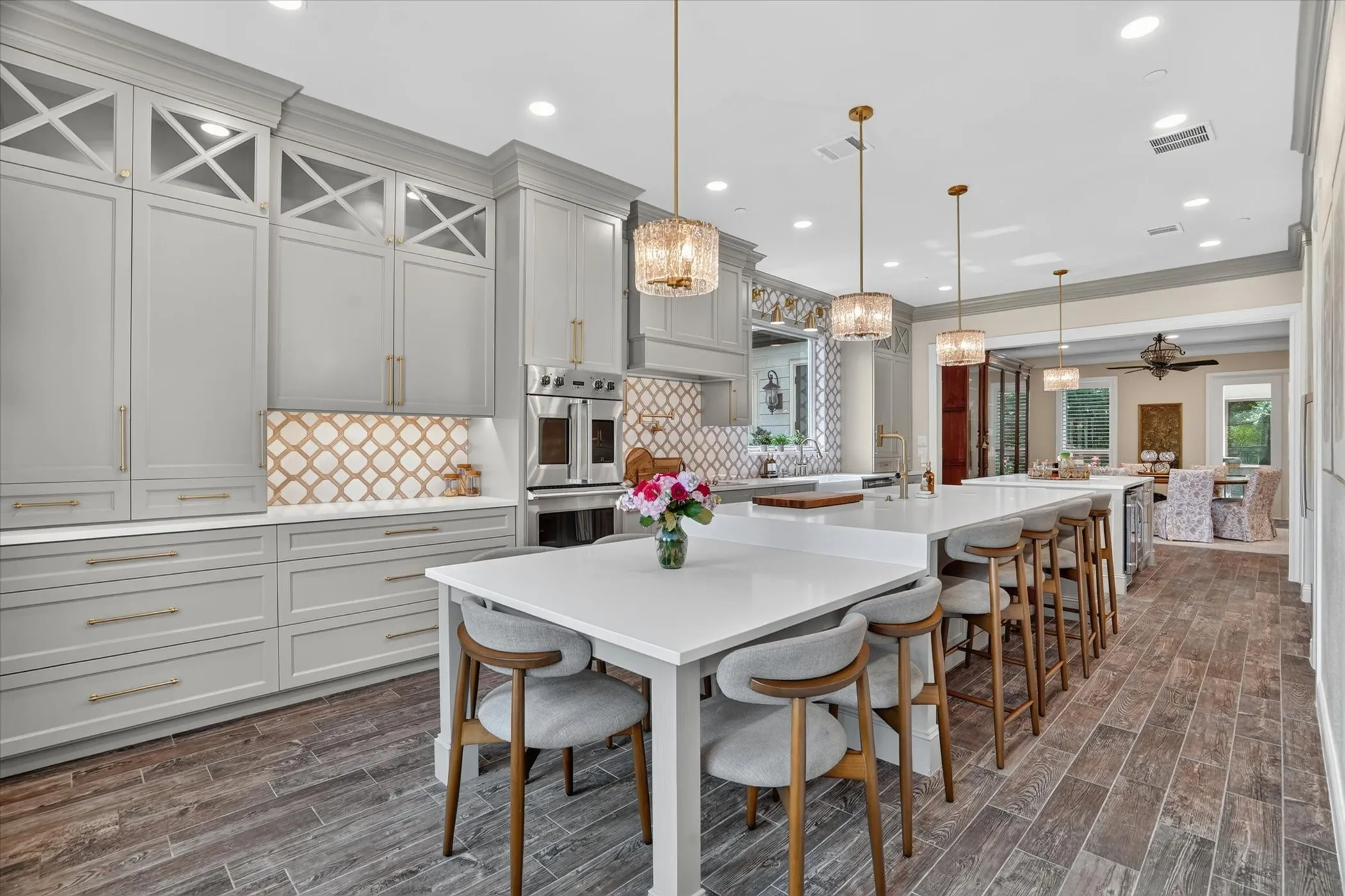 Expansive kitchen featuring light gray cabinetry with gold hardware, a patterned backsplash, and stainless steel built-in appliances