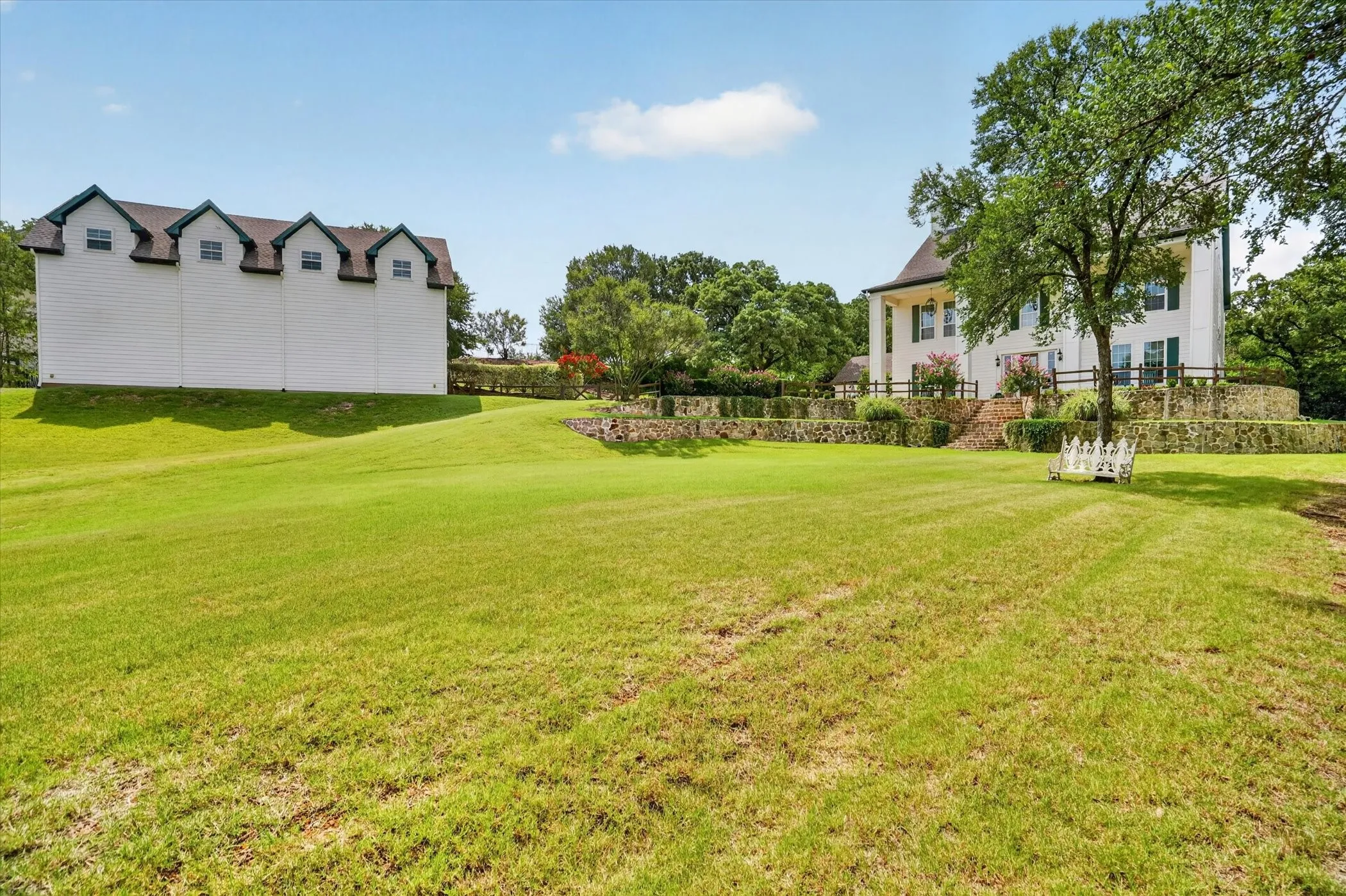 Expansive lawn area featuring a large white main residence with dark green shutters, a separate white multi-dormer building, and a stone retaining wall