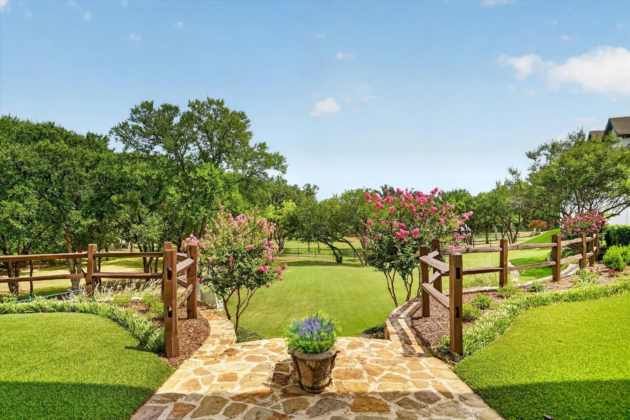 Expansive outdoor space featuring a flagstone pathway, manicured lawn, tiered landscaping, and mature trees