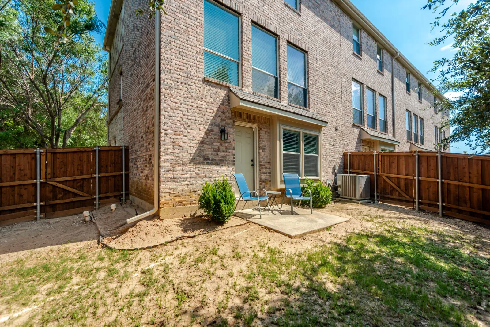 Brick exterior featuring multiple tall windows with dark frames, a private patio, and a wooden privacy fence
