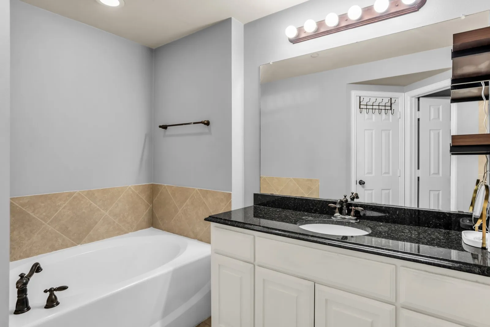 Bathroom vanity with a dark granite countertop, undermount sink, and bronze faucet