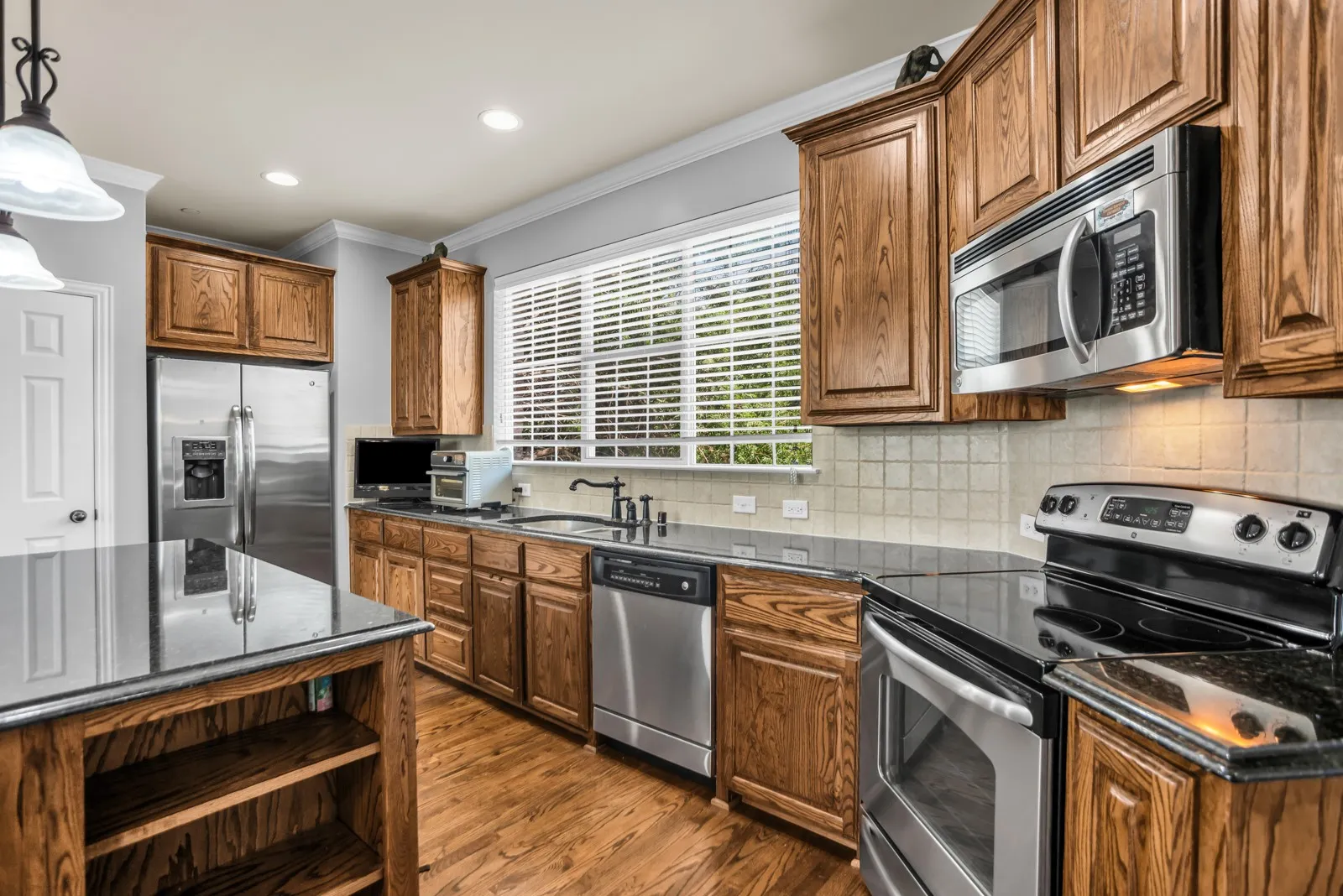 Kitchen featuring wood cabinetry, dark countertops, stainless steel appliances, and wood-finish flooring