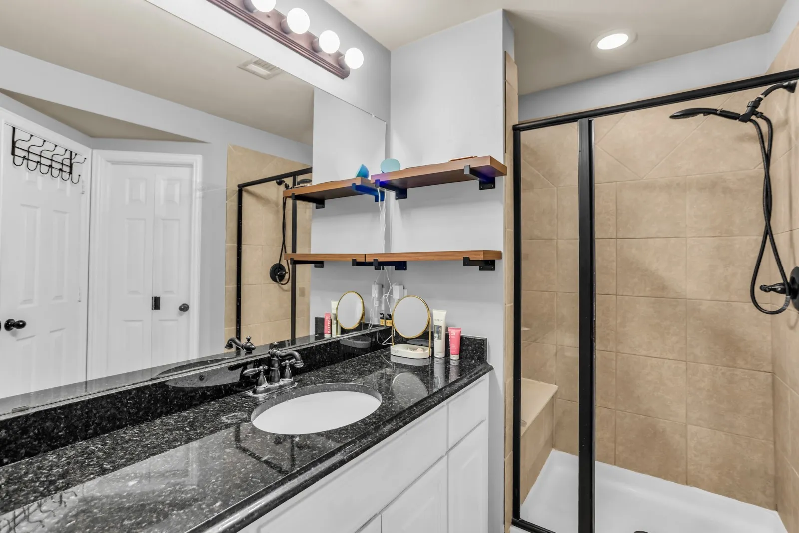 Bathroom featuring a black granite-look countertop, white vanity cabinet, and a framed glass shower enclosure