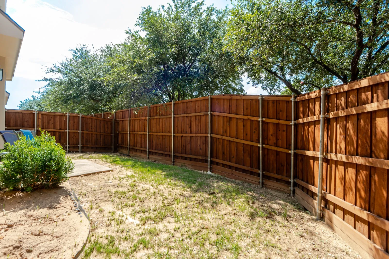 Expansive backyard featuring a stained wood privacy fence, a concrete patio area, and mature trees providing natural shade