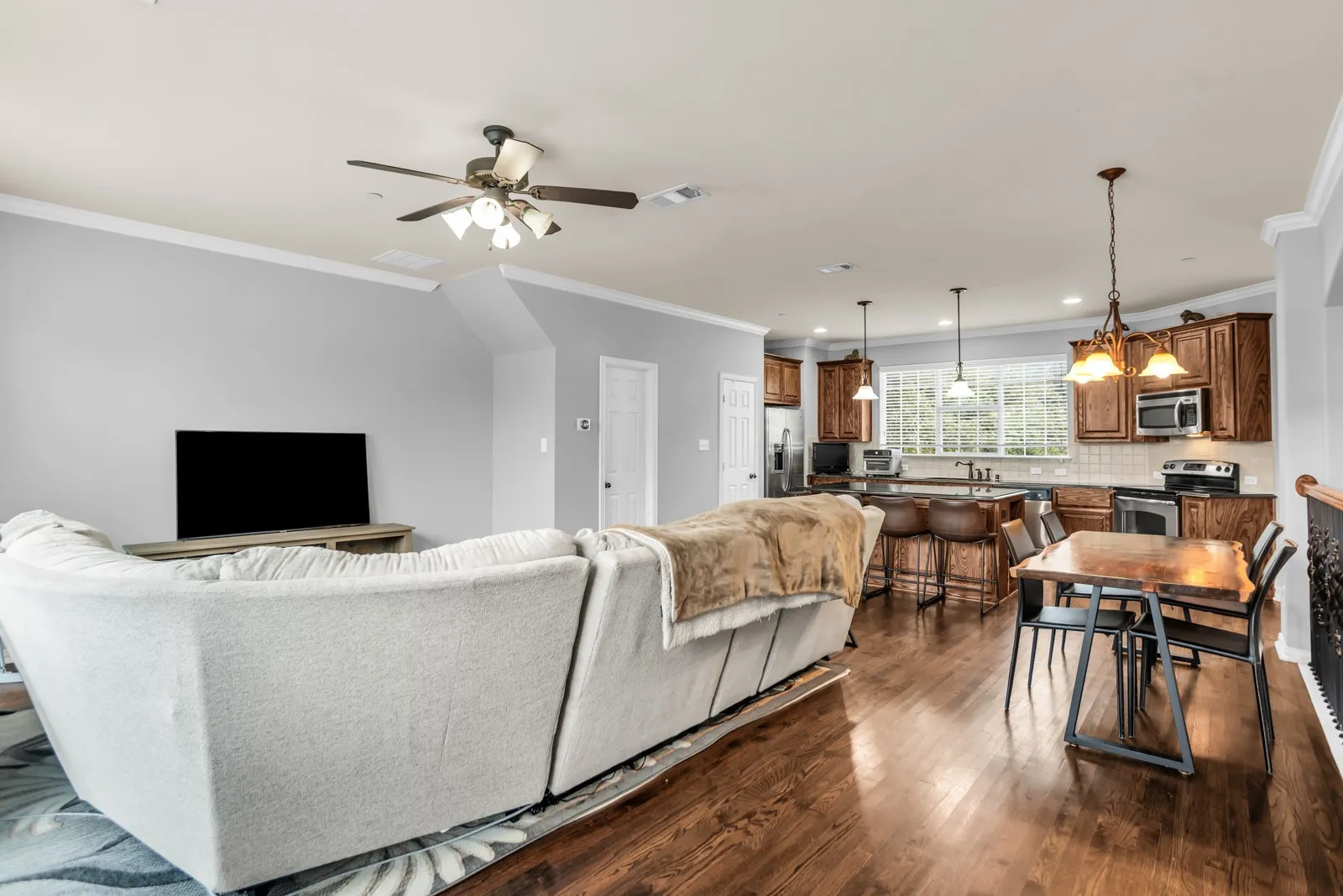 Open-concept living area featuring rich wood-finish flooring, a contemporary ceiling fan, and crown molding