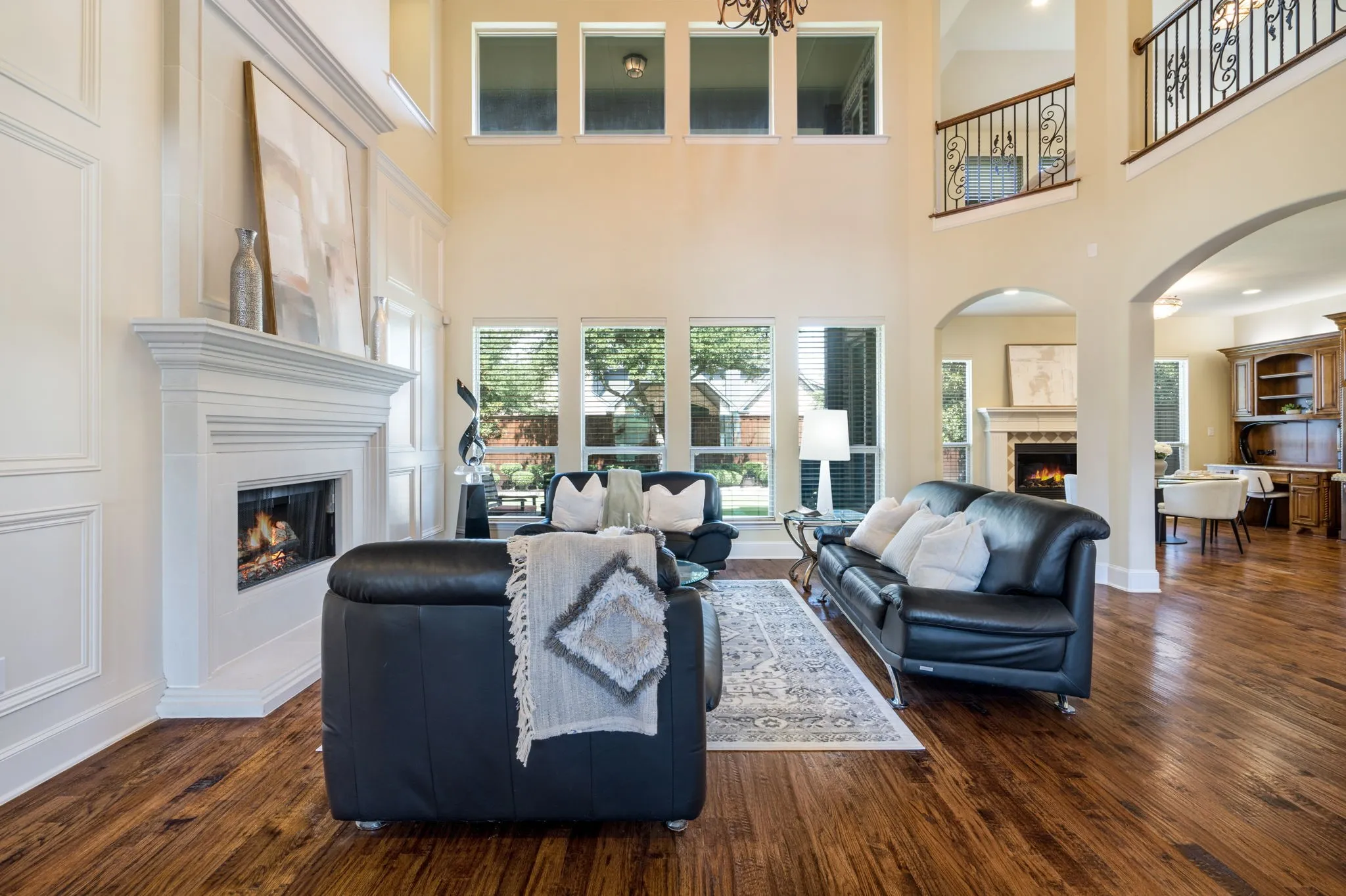 Two-story living area with hardwood flooring, a fireplace featuring a white mantel, and extensive window treatments