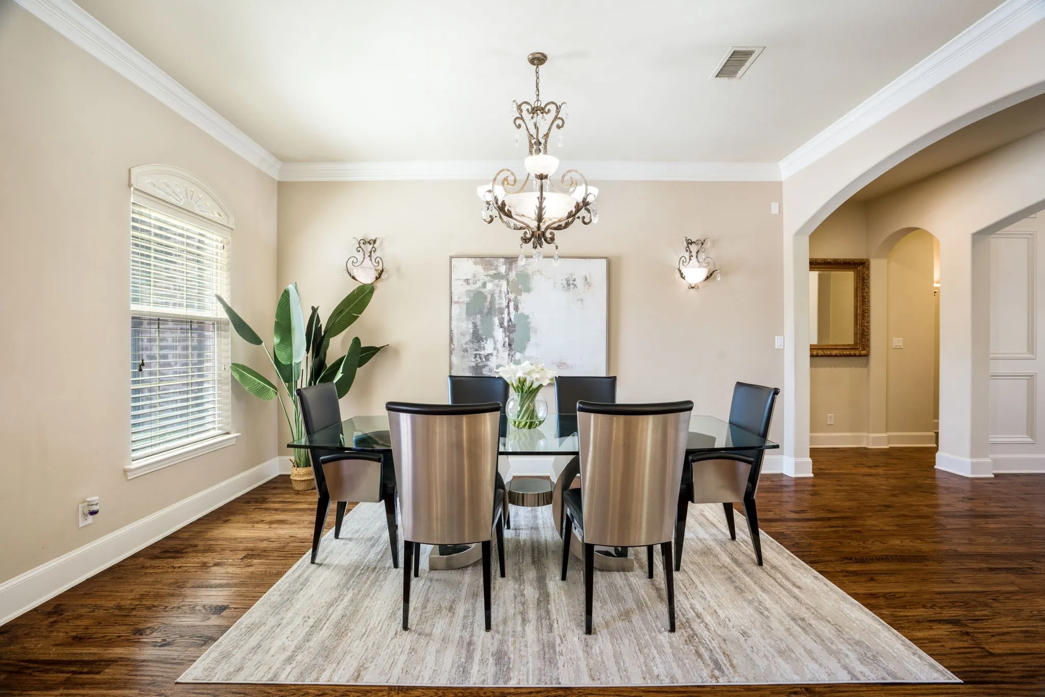 Hardwood-finish flooring, crown molding, arched entryways, and a chandelier with coordinating sconces