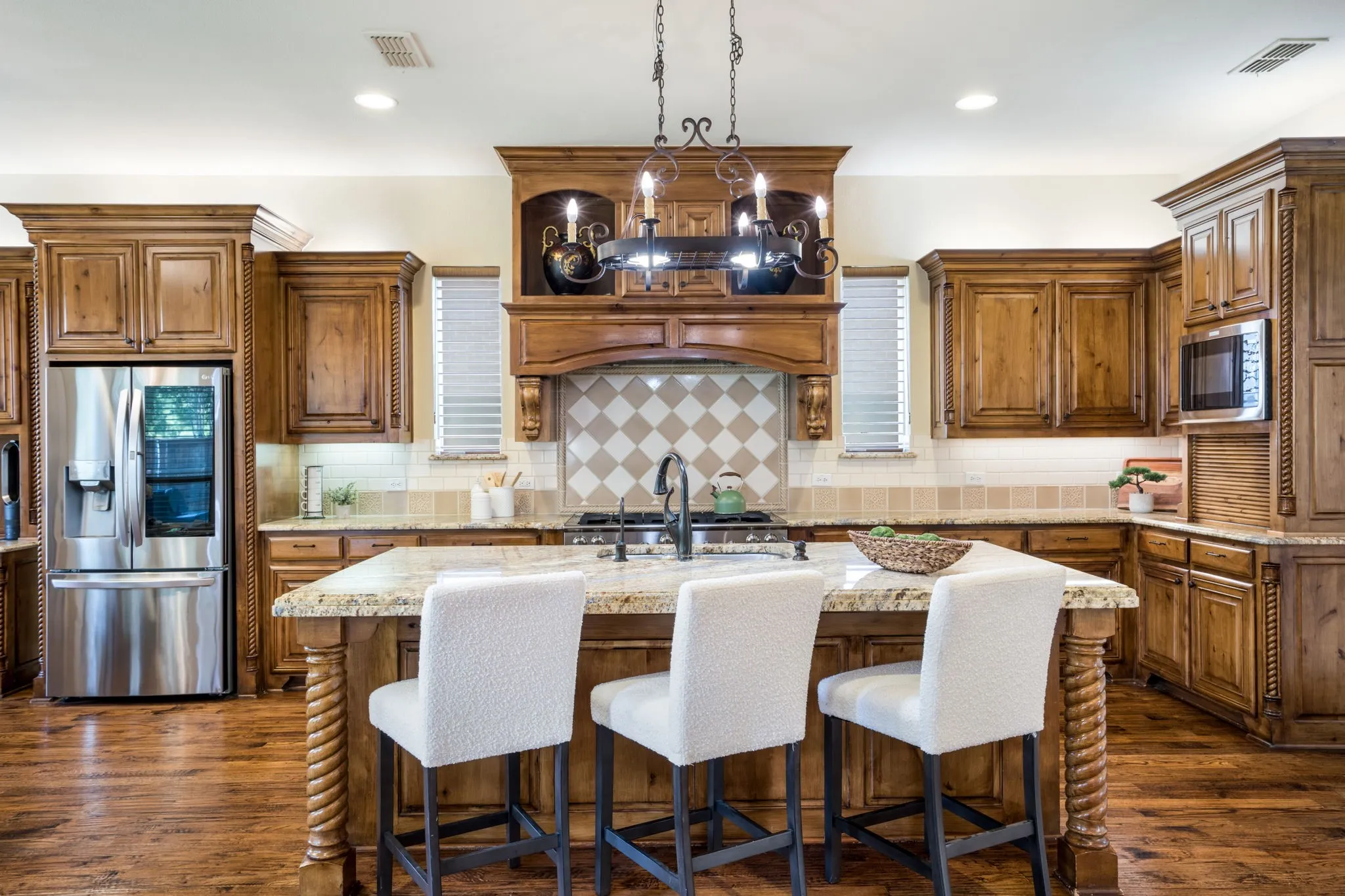 Spacious kitchen featuring extensive wood cabinetry, stainless steel appliances, a large island with a stone countertop, and a decorative range hood