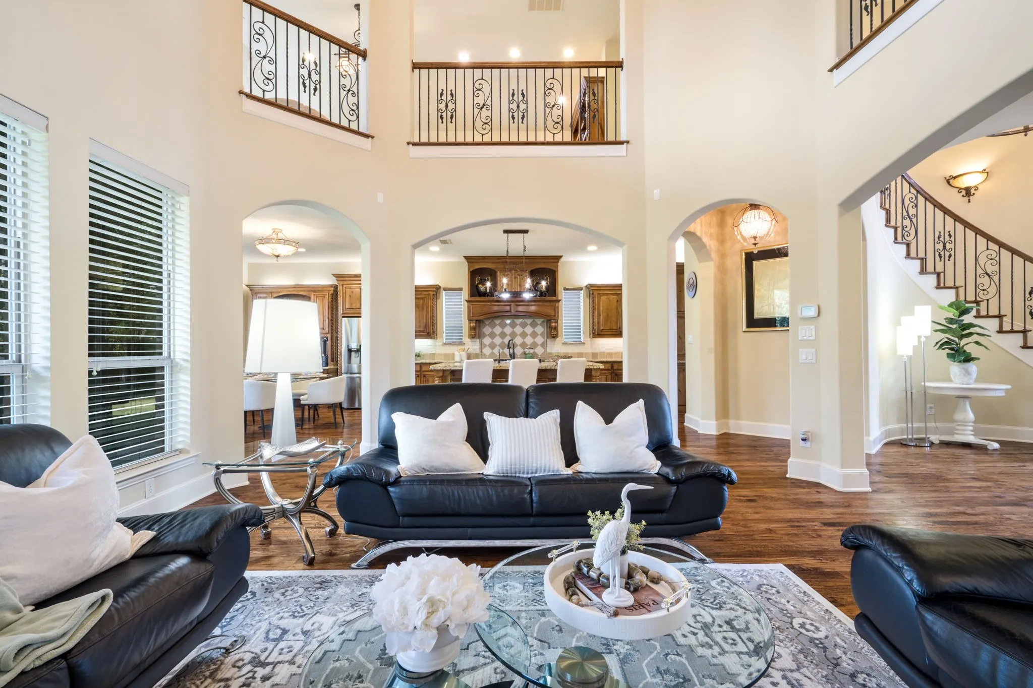 Two-story living area with wood-finish flooring, arched doorways, and upper-level balconies featuring wrought iron railings
