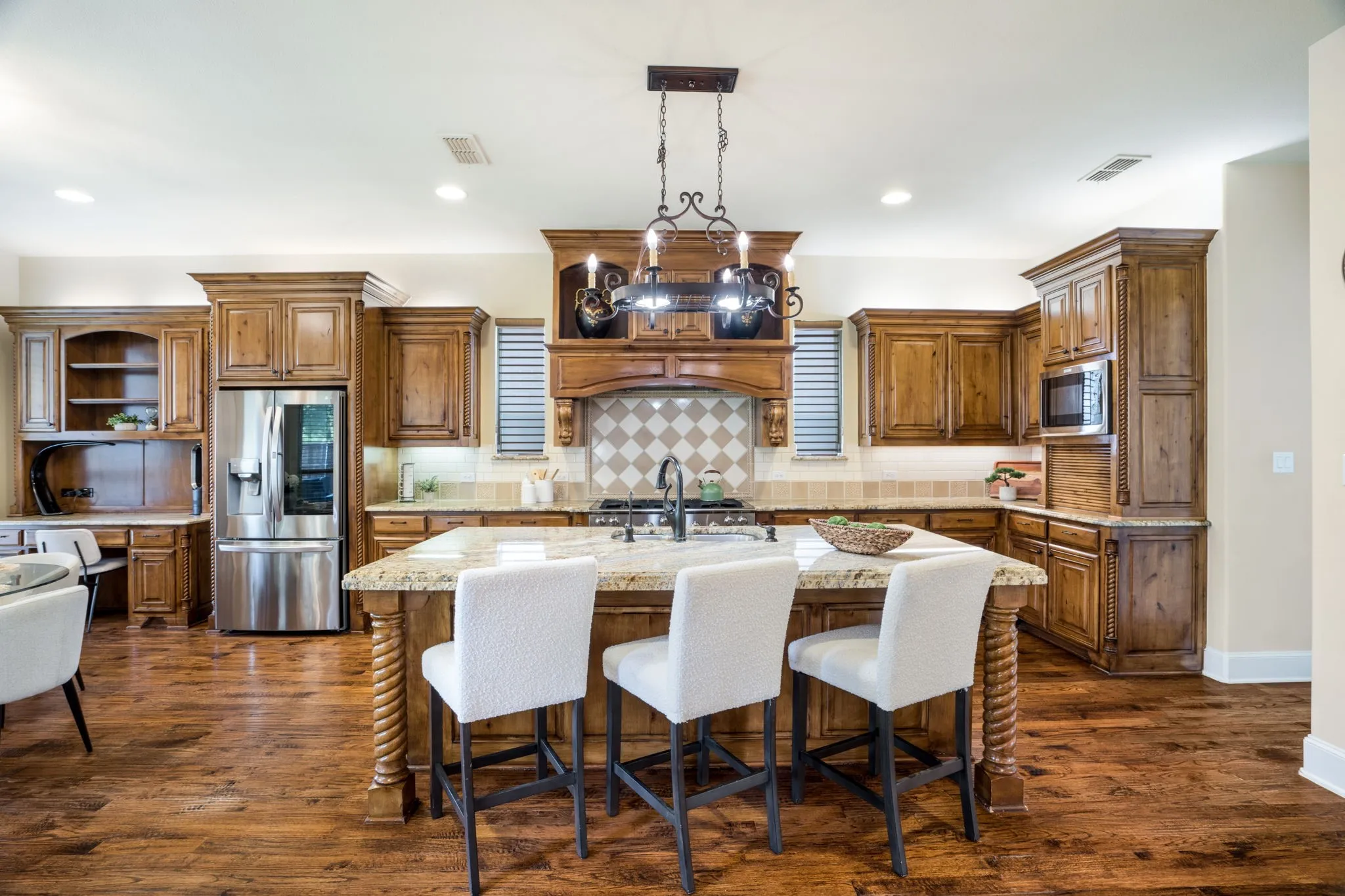 Wood-finish flooring, custom wood cabinetry, stainless steel refrigerator, built-in microwave, and a decorative kitchen island with a stone countertop