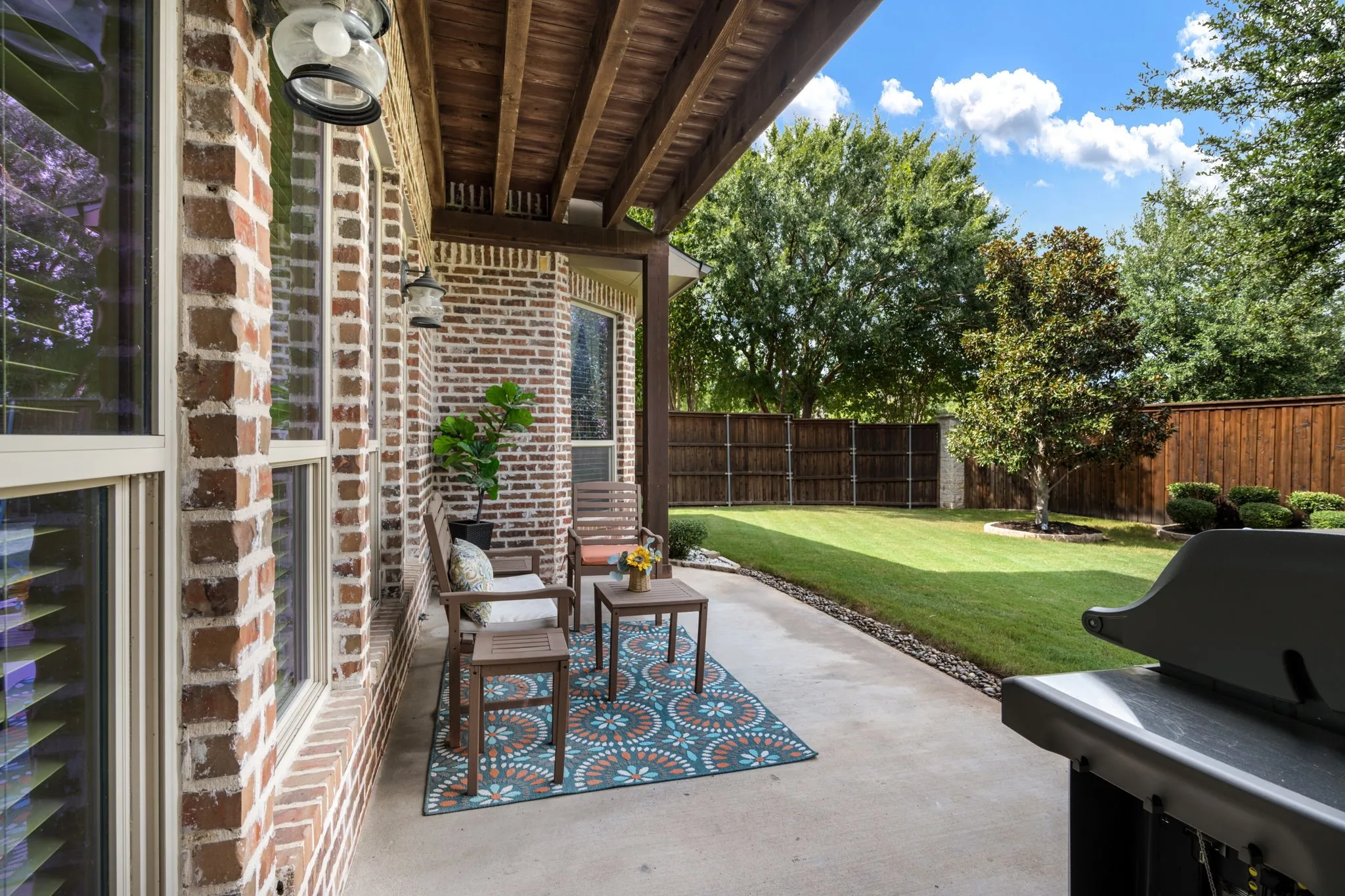 Covered patio featuring brick exterior walls and architectural wood beams