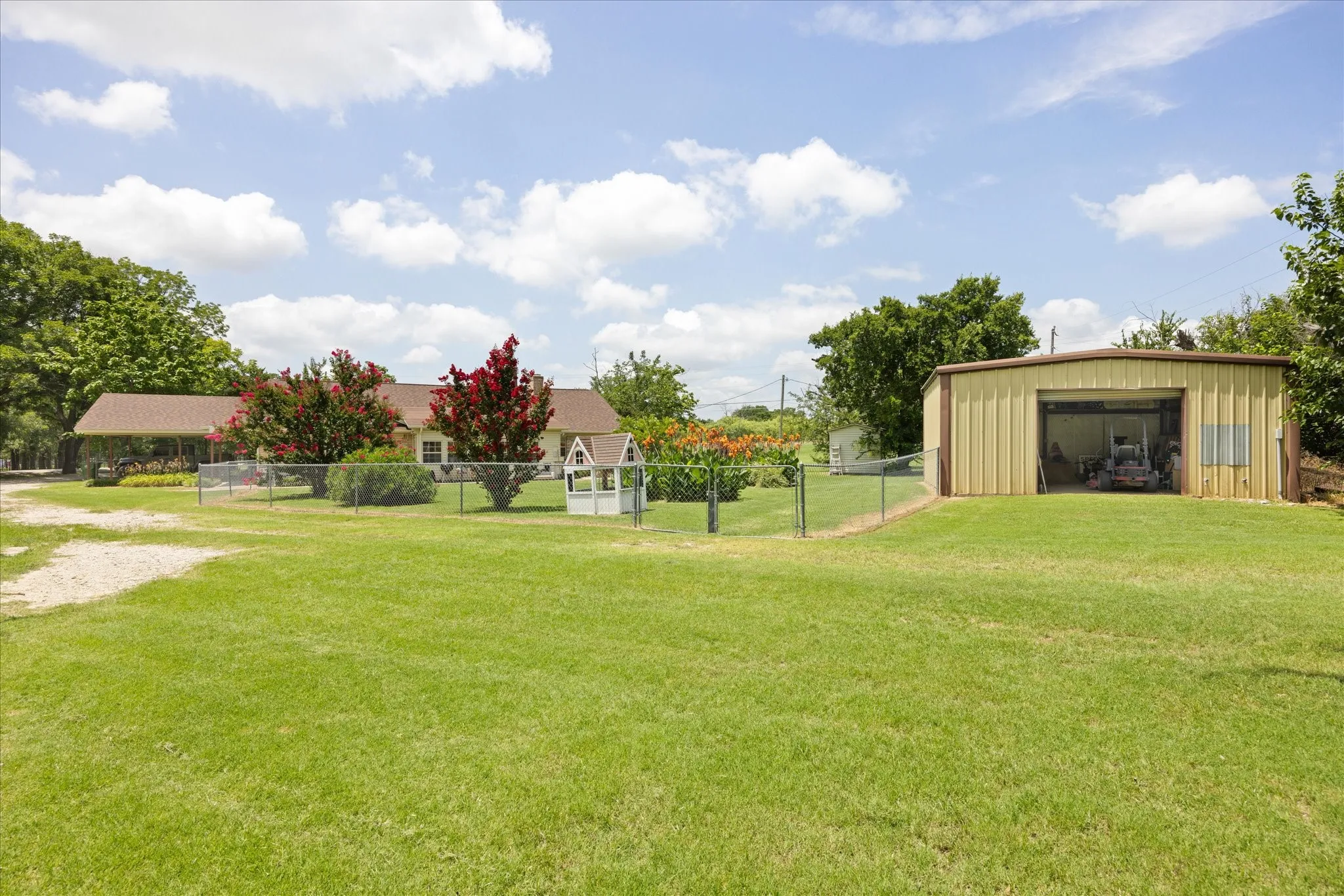 Expansive green lawn with a chain-link fence, detached metal storage building, and a single-story residence featuring a covered porch